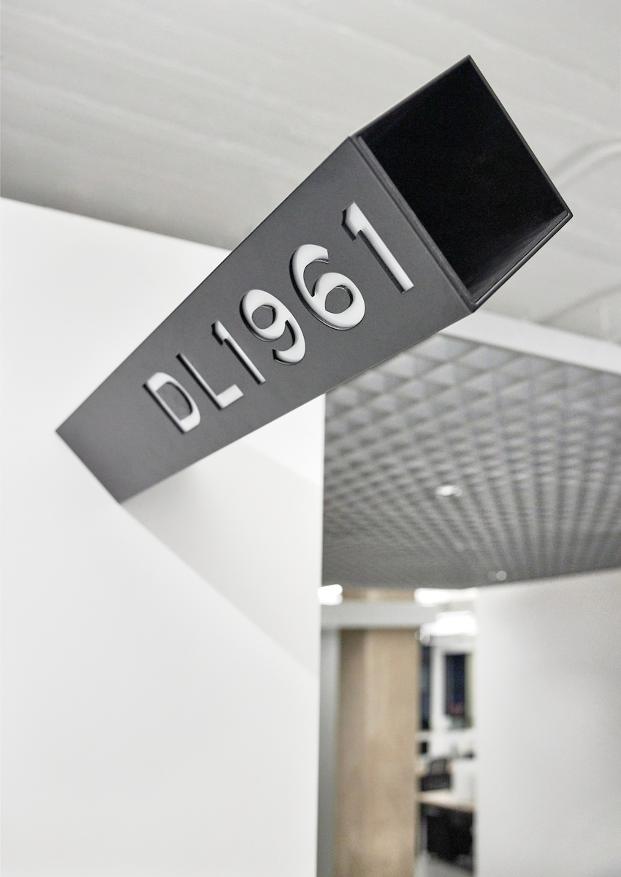 Close-up of angled black metal wayfinding sign with raised lettering mounted on white ceiling