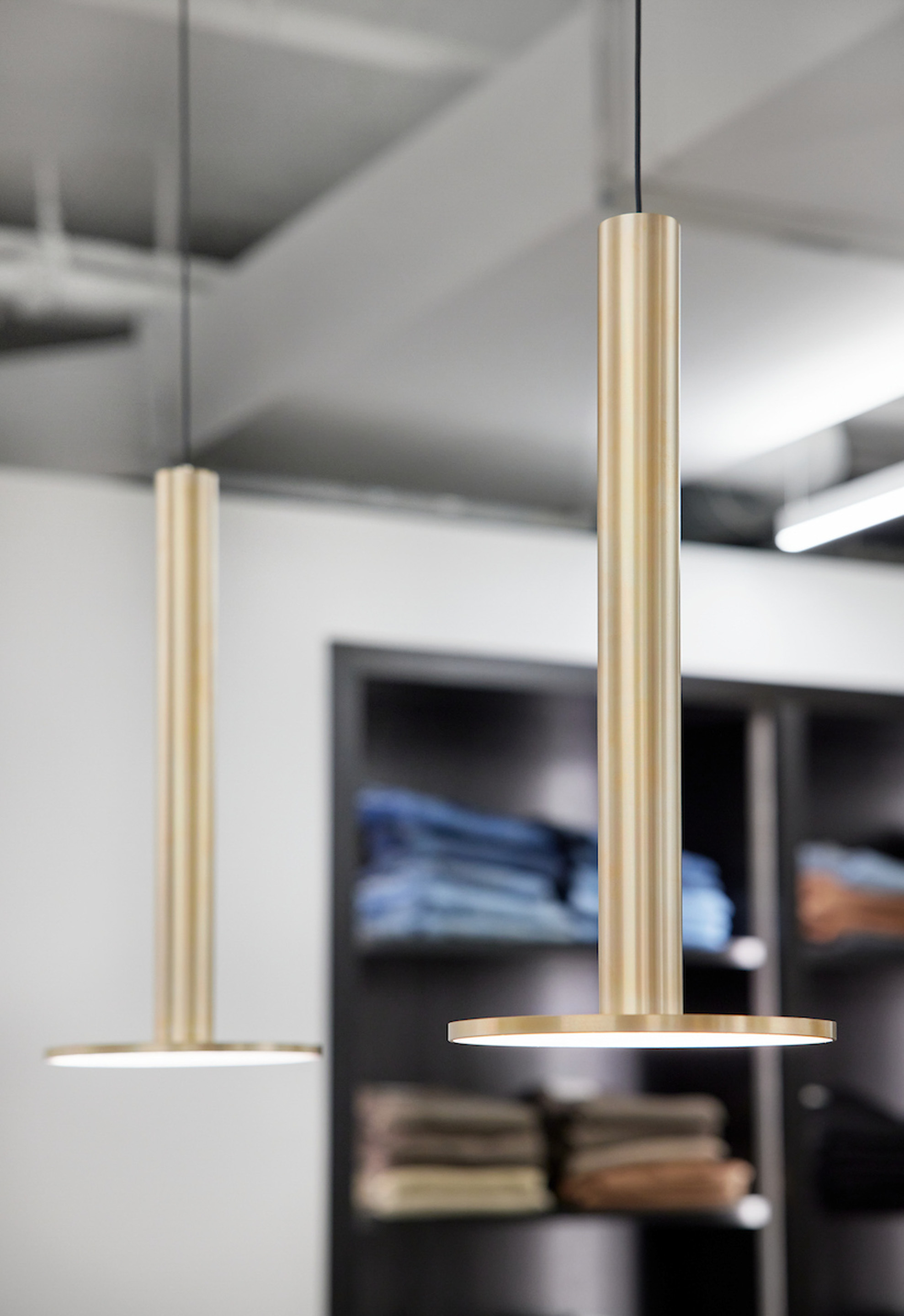 Pair of brass cylindrical pendant lights hanging above retail display shelving in background