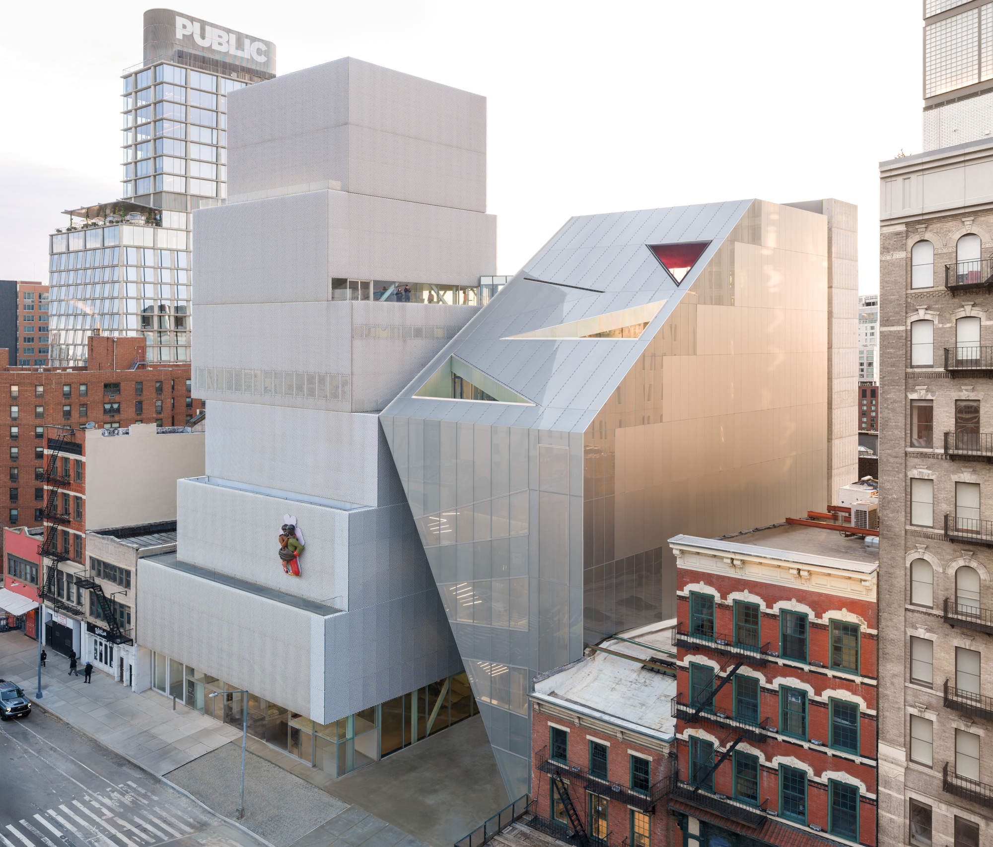 Aerial view of the stacked zinc-clad volumes rising above neighboring brick buildings in afternoon light