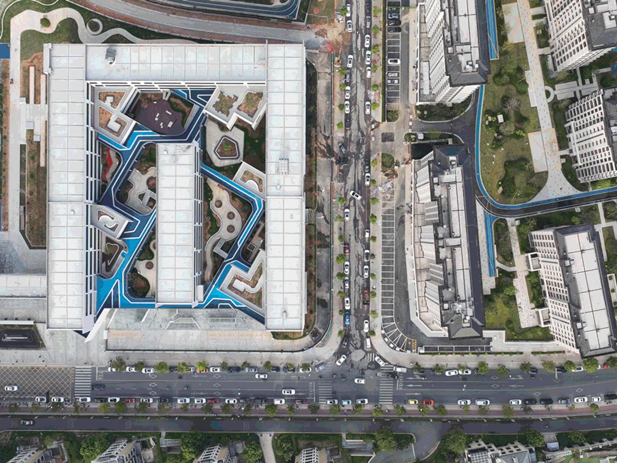 Drone view of rooftop with blue courtyard pattern surrounded by city streets and traffic