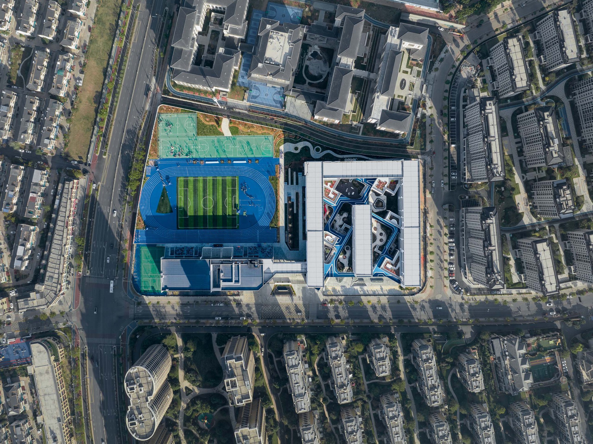 Aerial view of the campus with blue running track and rooftop sports field surrounded by urban blocks