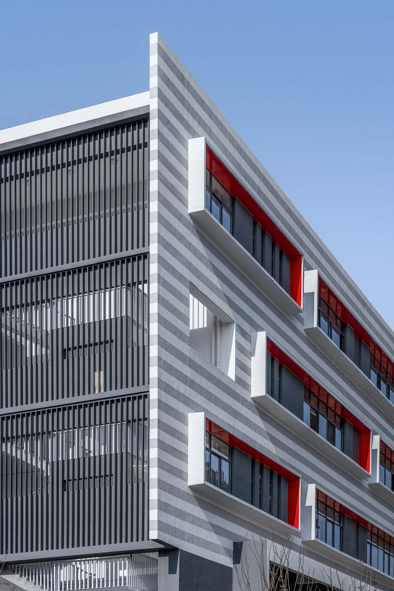 Facade detail showing vertical louver screens beside horizontal grey and white striping with red window frames