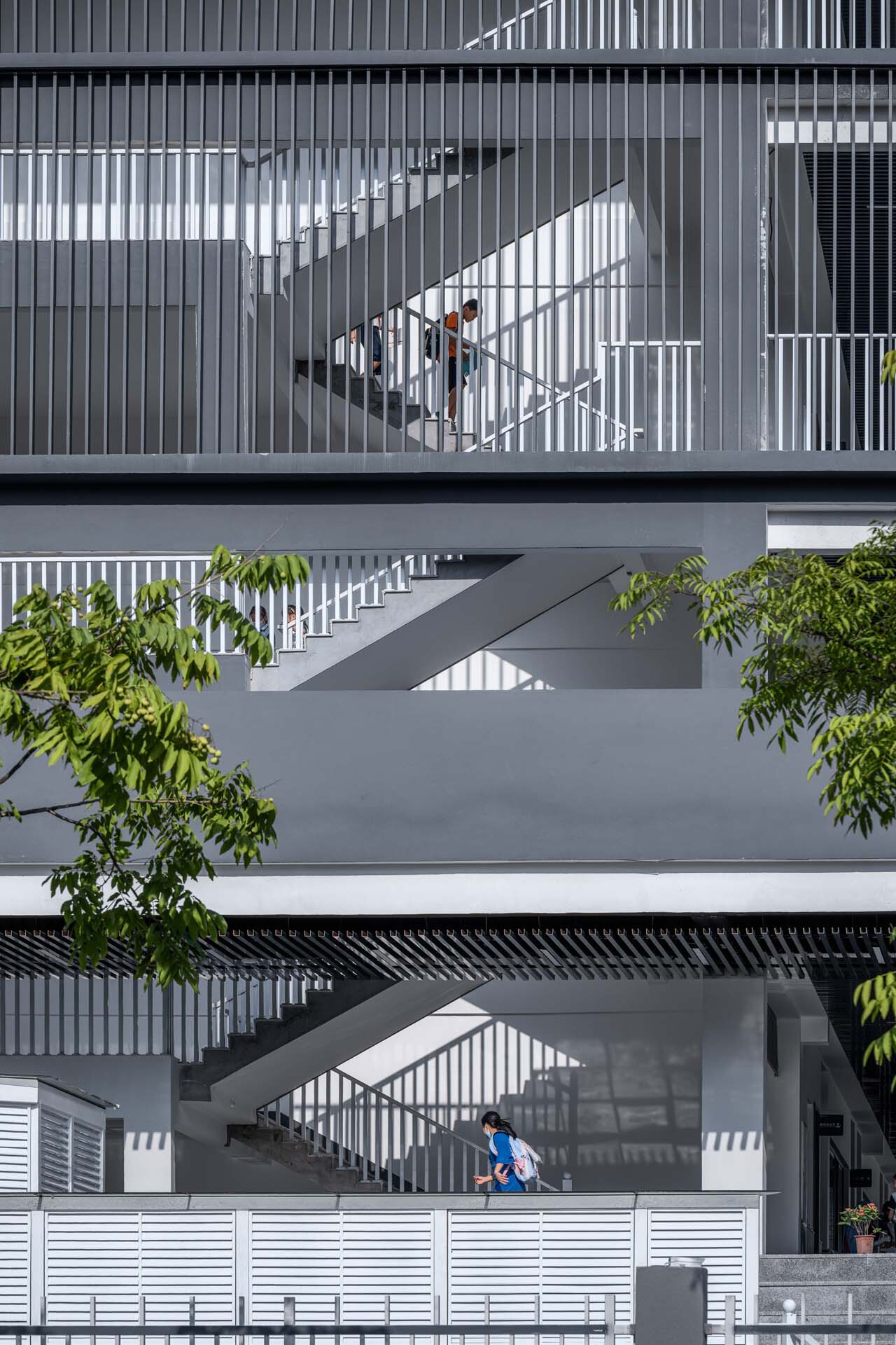 Stacked exterior staircases with vertical metal screening creating shadow patterns as a child descends