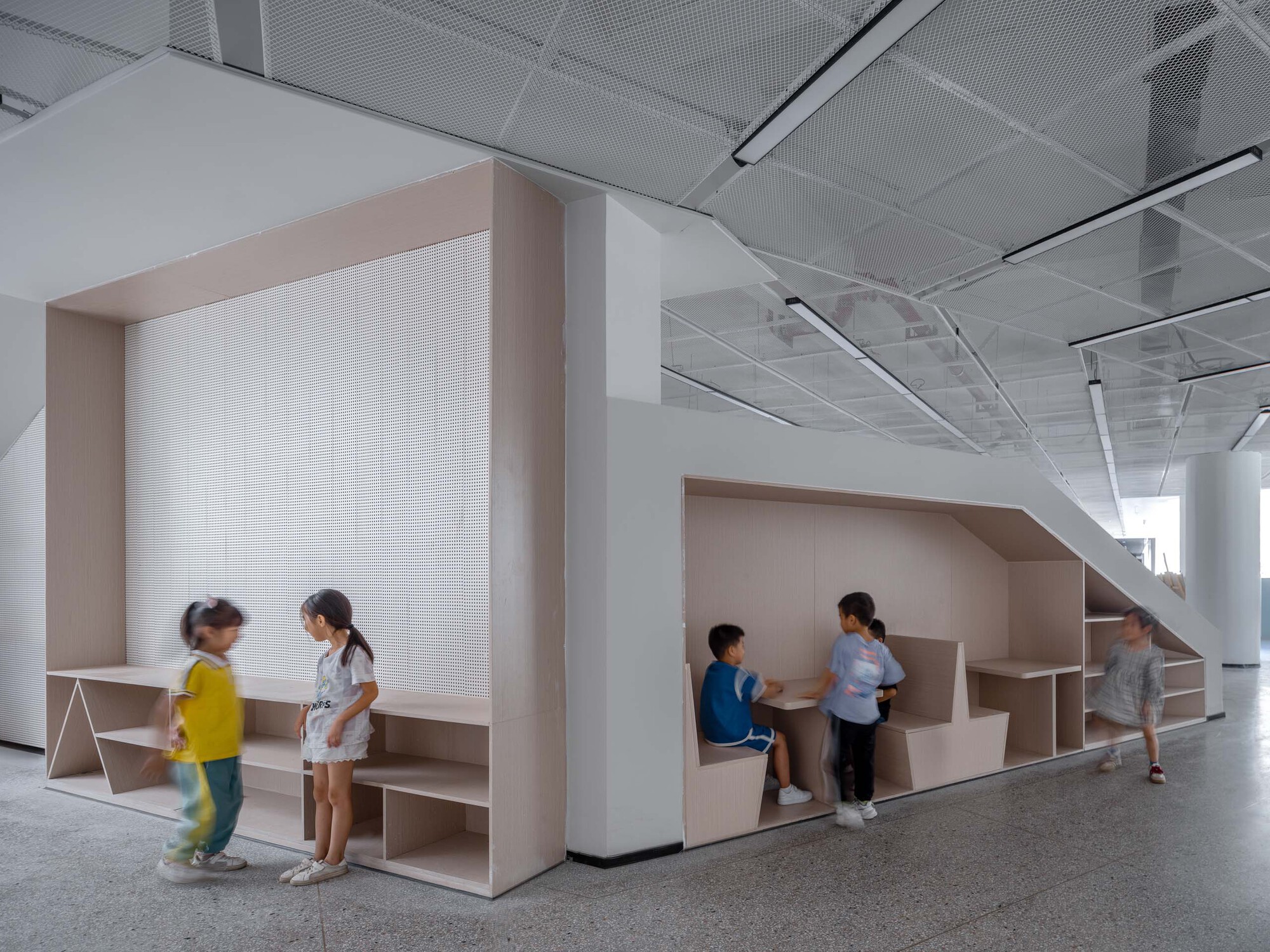 Library alcoves with pale wood frames and translucent screens under a perforated metal ceiling with children gathered