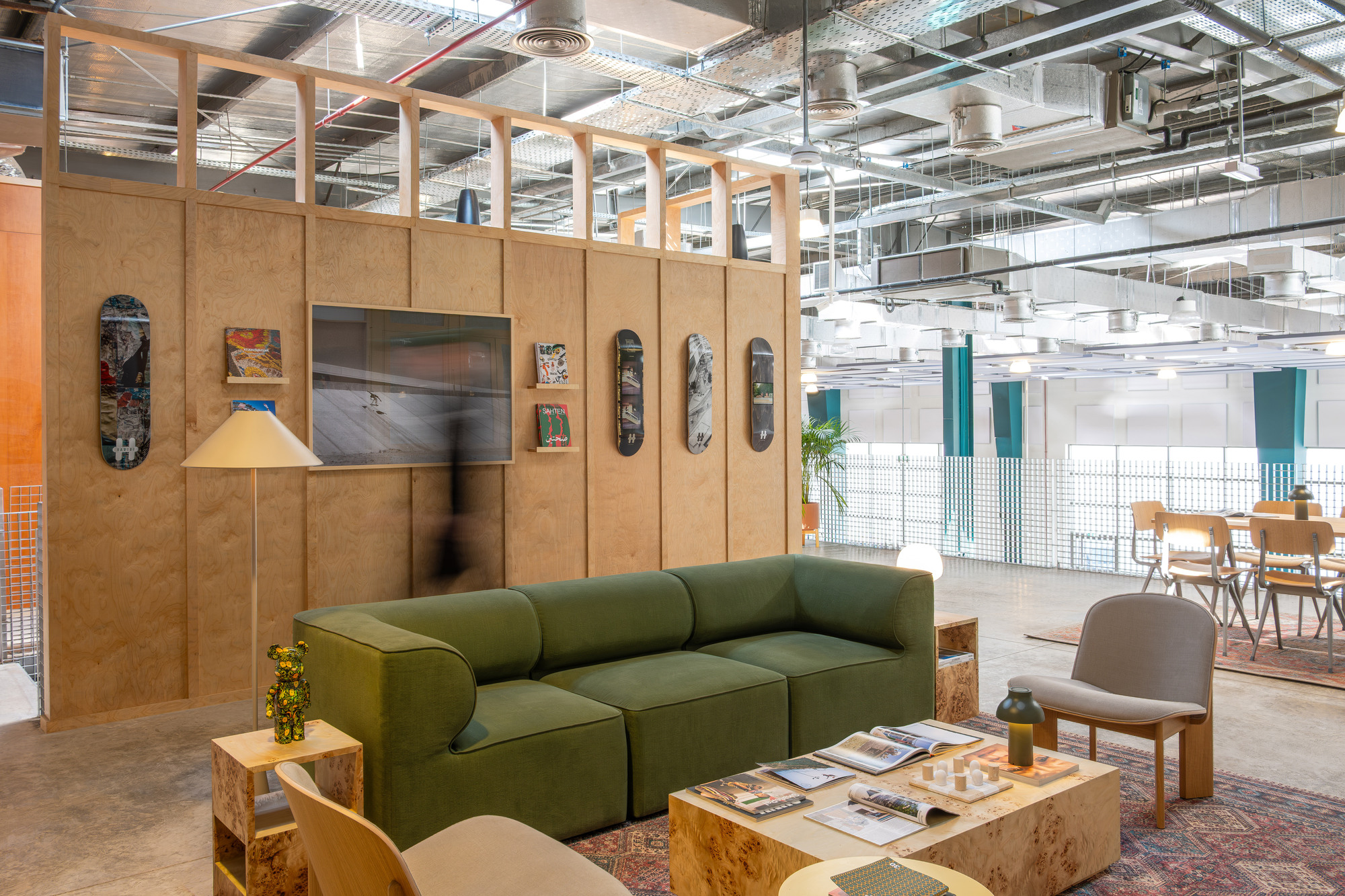 Plywood partition wall displaying skateboards and artwork with exposed ceiling infrastructure beyond