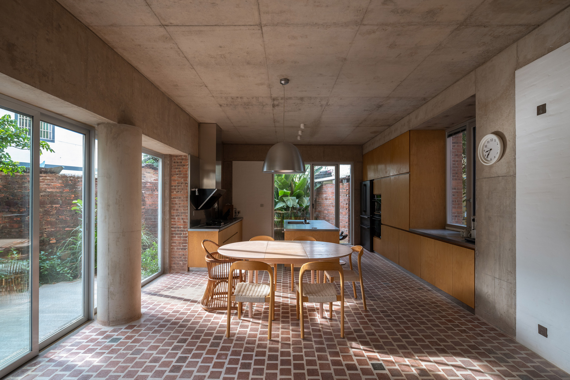Open-plan kitchen and dining area with exposed concrete ceiling and terracotta tile floor under afternoon sunlight