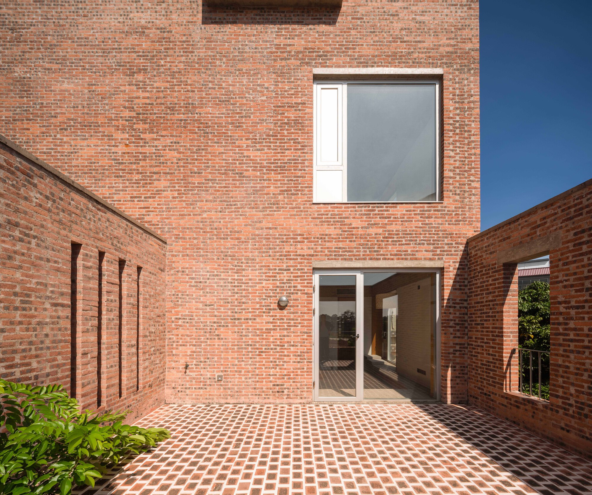 Brick courtyard with chequered paving leading to glass doors under a square window with partial screening
