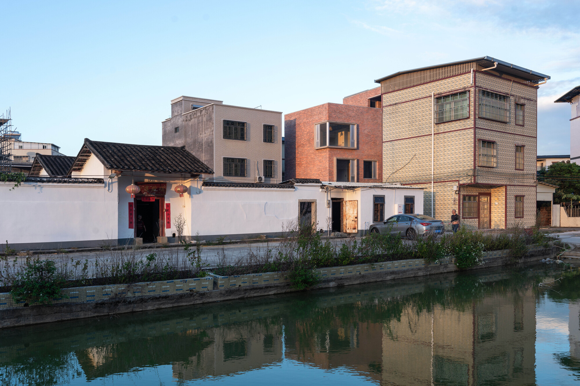 Multi-story brick facade rising among older neighborhood buildings reflected in the canal at dusk