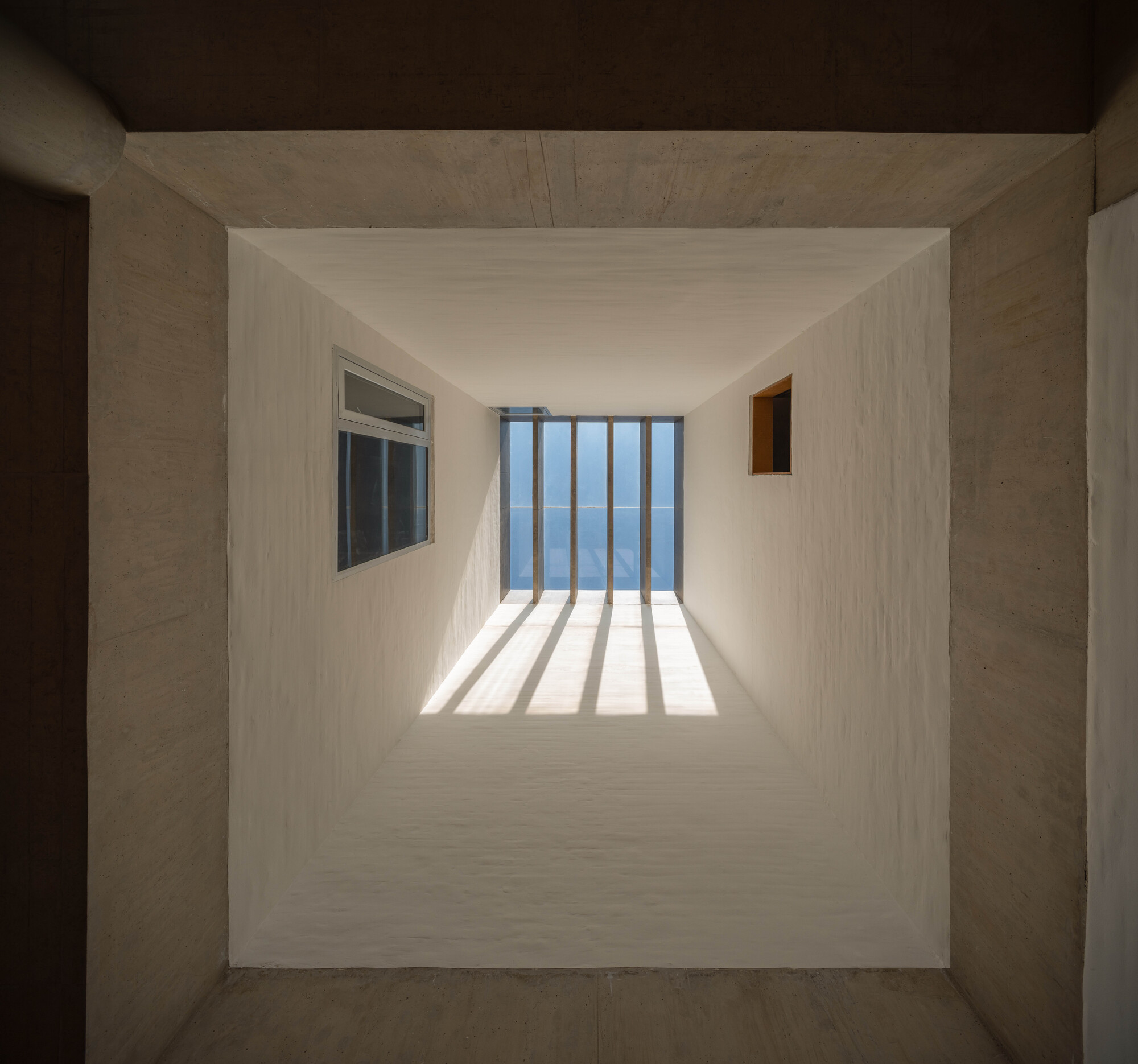 Looking up through a skylight shaft with vertical louvers casting striped shadows on white plaster walls