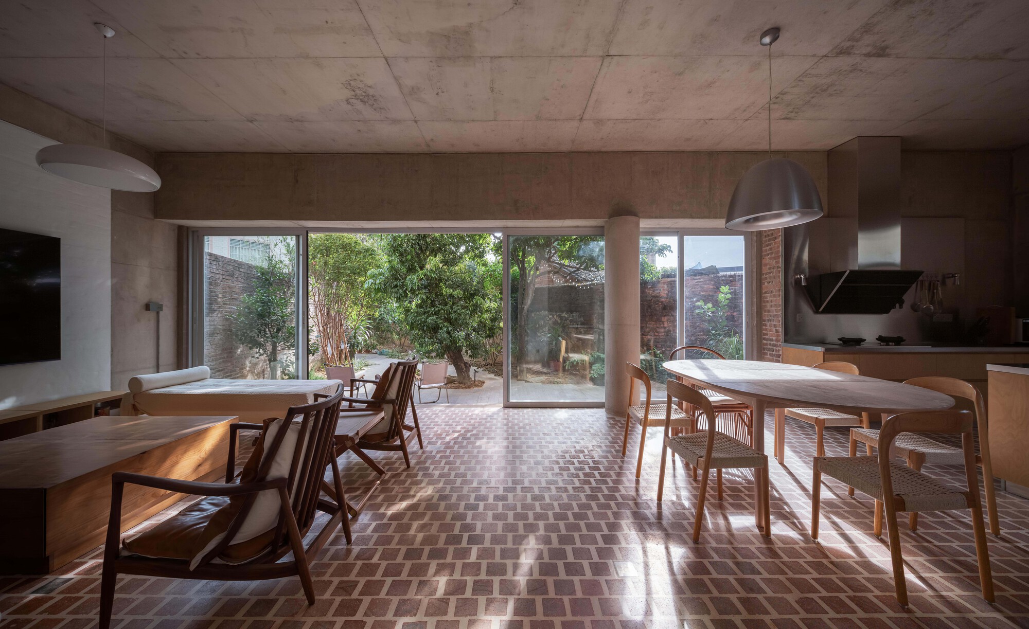 Open plan dining and living space with patterned tile floor and full-height glazing opening to a planted courtyard