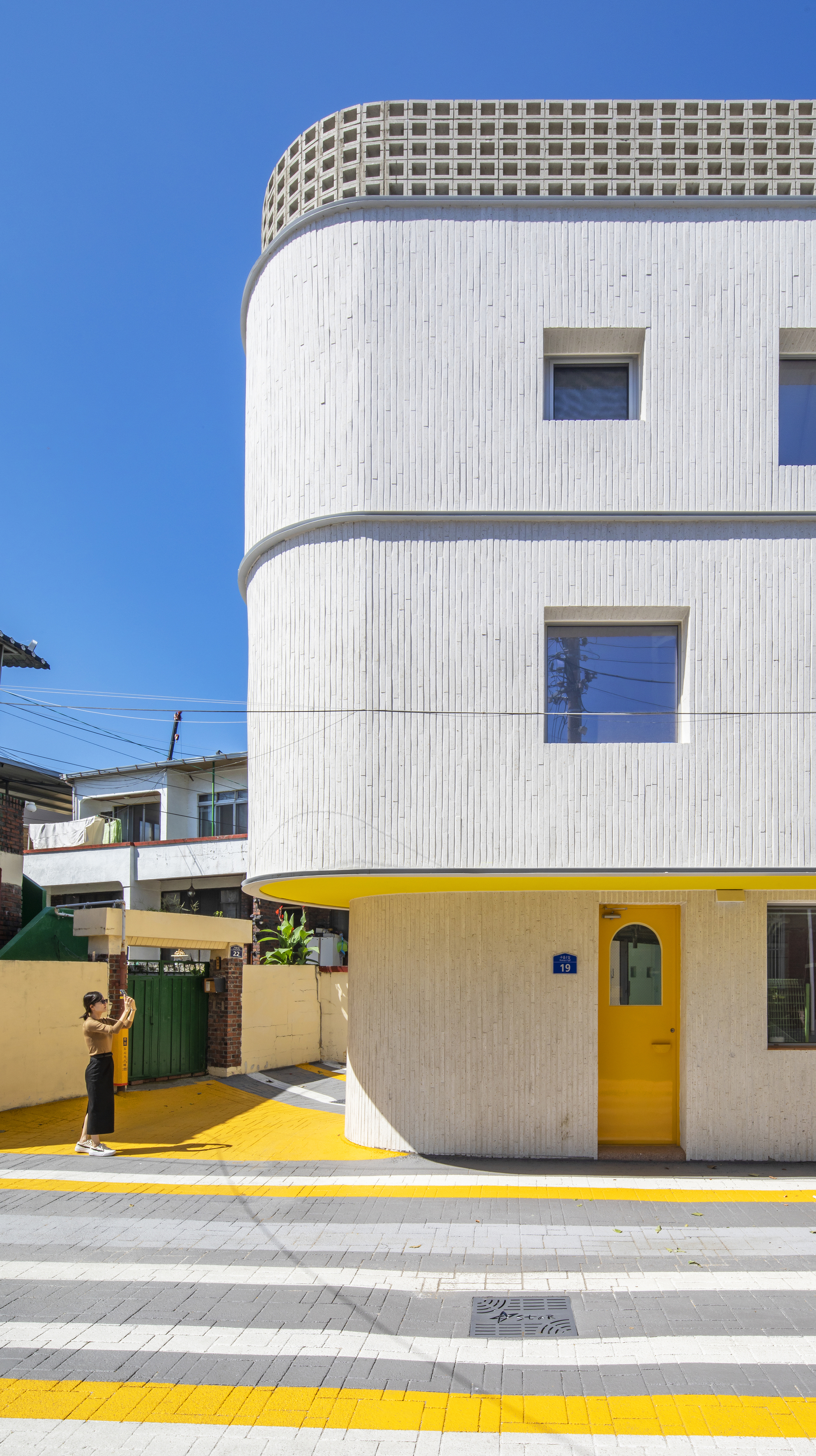 Street view of the white cylindrical tower with yellow door and crosswalk as a person approaches