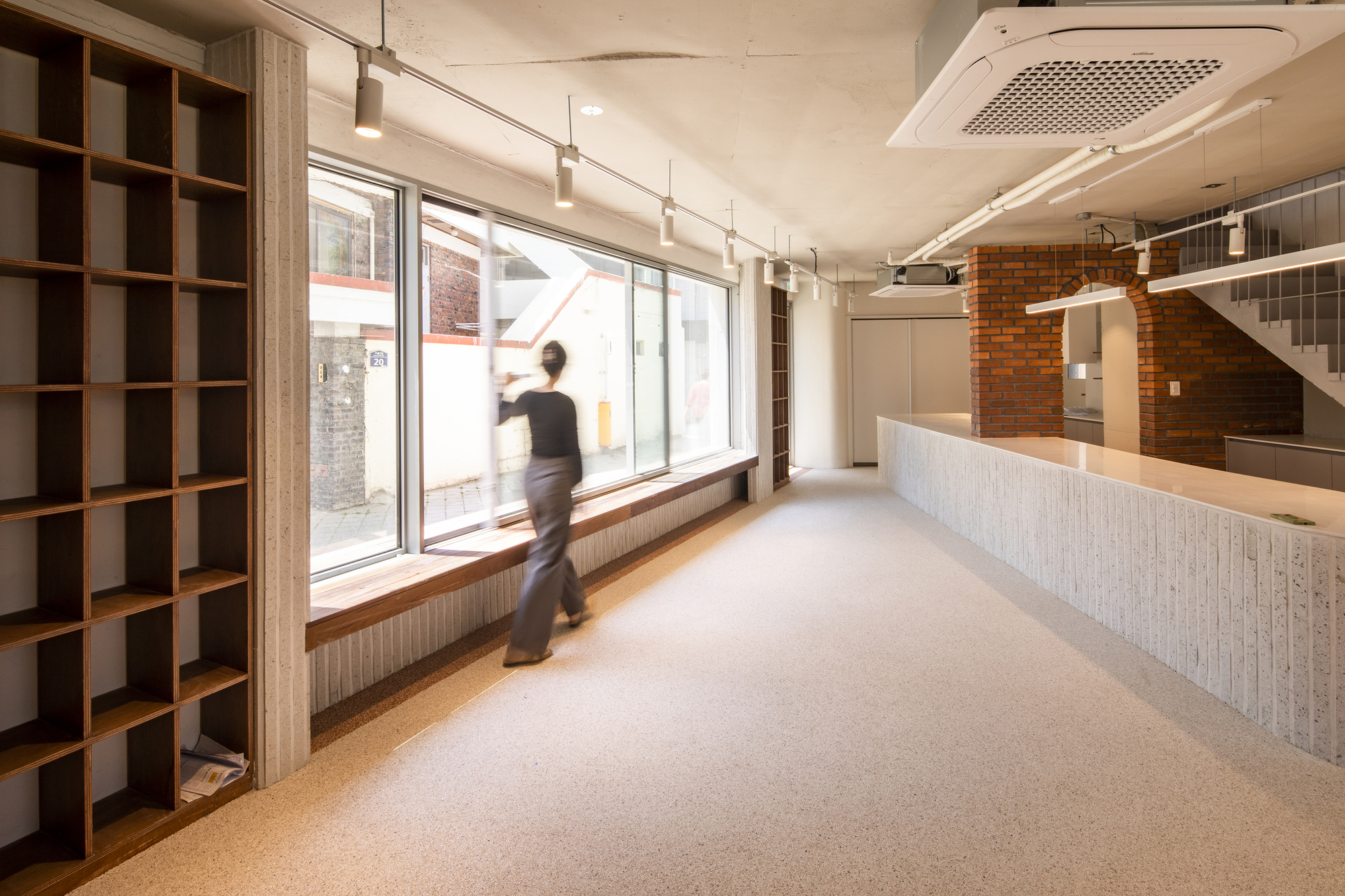 Interior ground floor with ribbed counter, exposed brick wall, and figure walking past the window