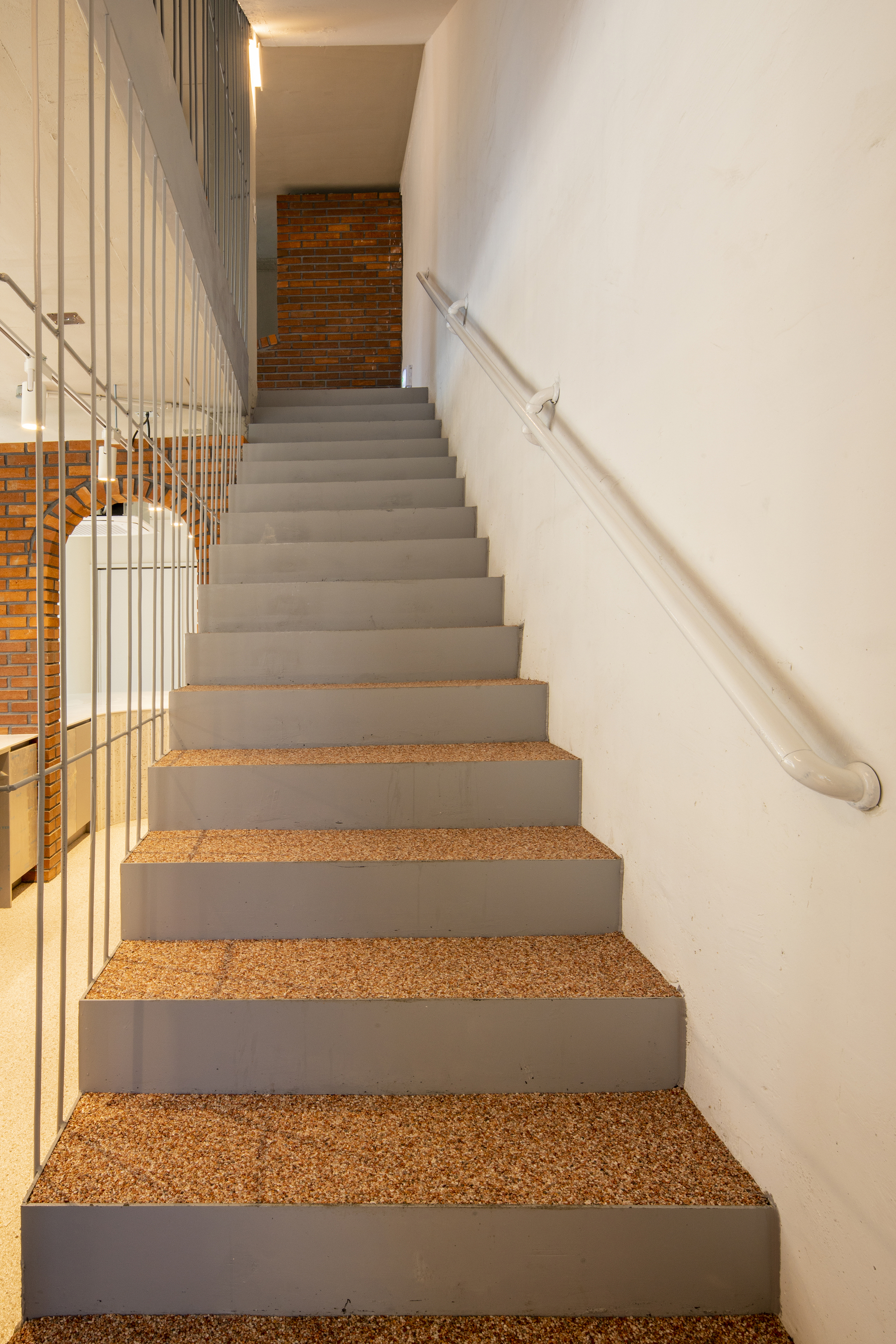 Concrete staircase with cork treads and metal handrail along white curved wall