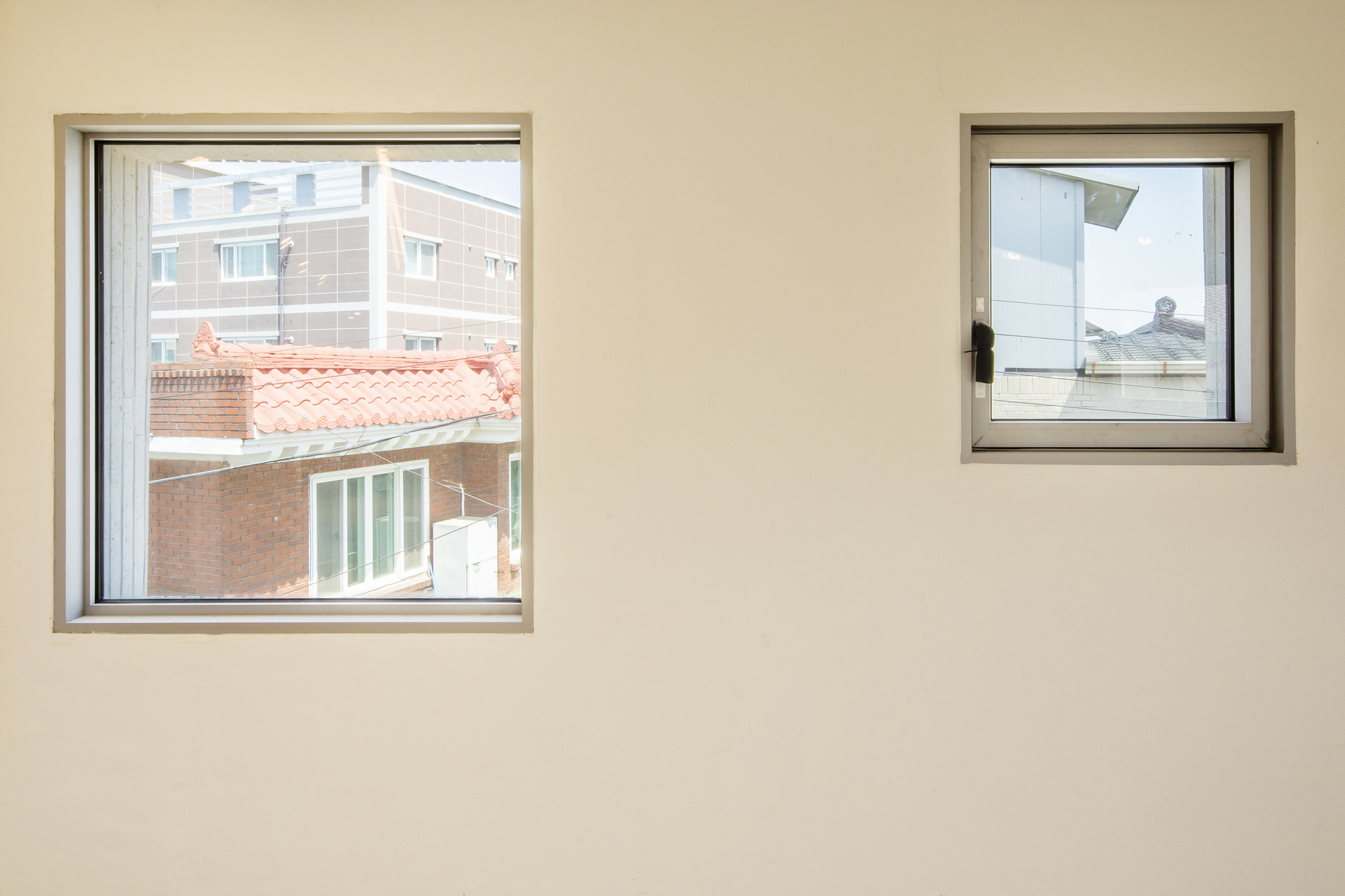 Two square windows in a white interior wall framing views of neighboring rooftops