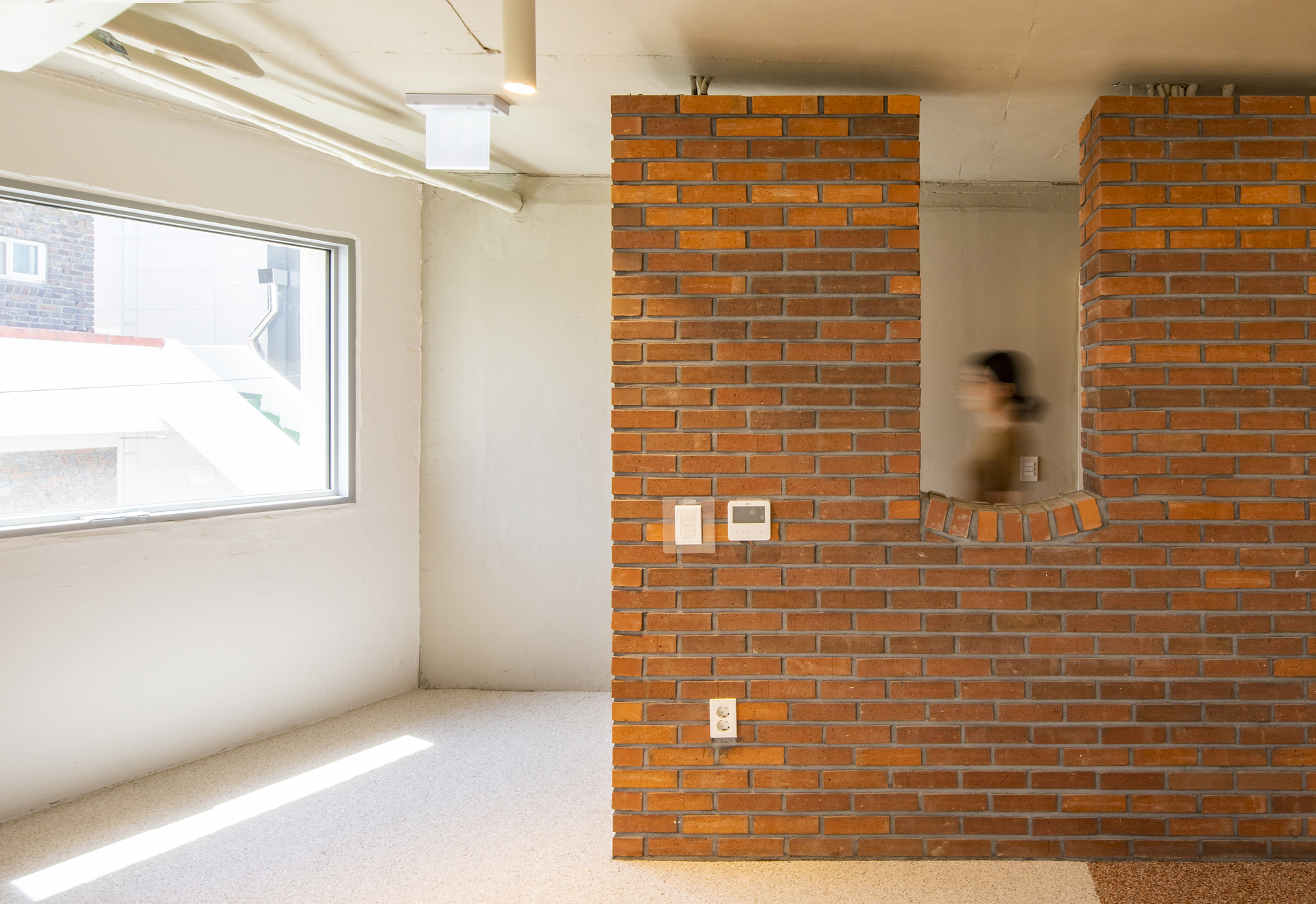 Orange brick partition wall with embedded controls as a figure passes through the sunlit space