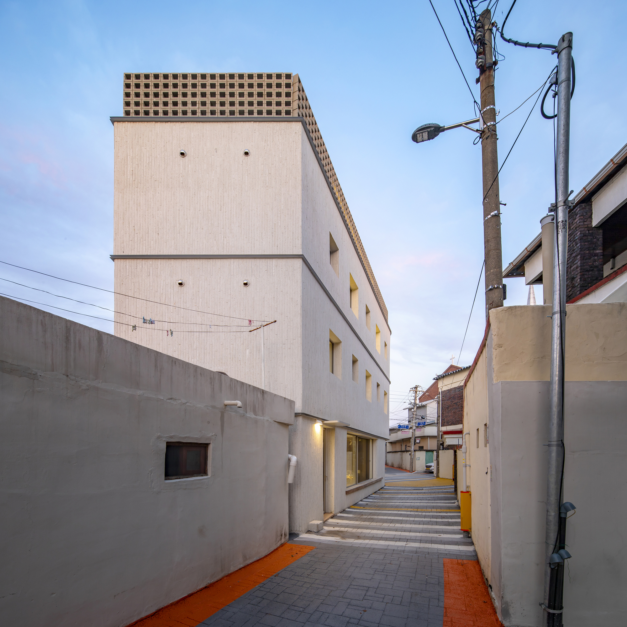 View down the shared alleyway with yellow and grey paving at dusk beneath overhead wires