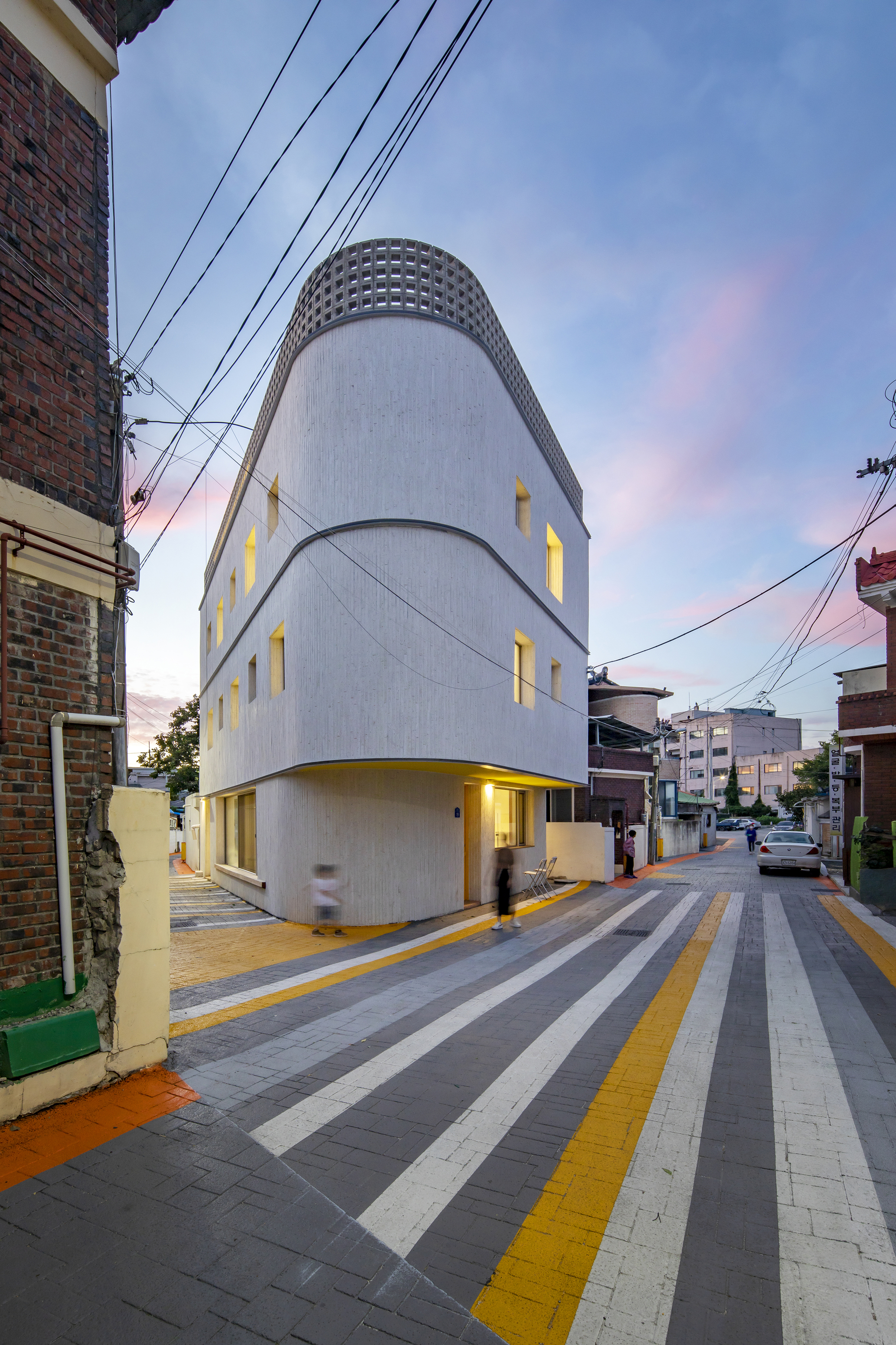 Three-story cylindrical volume with vertical window slots and illuminated interior at twilight