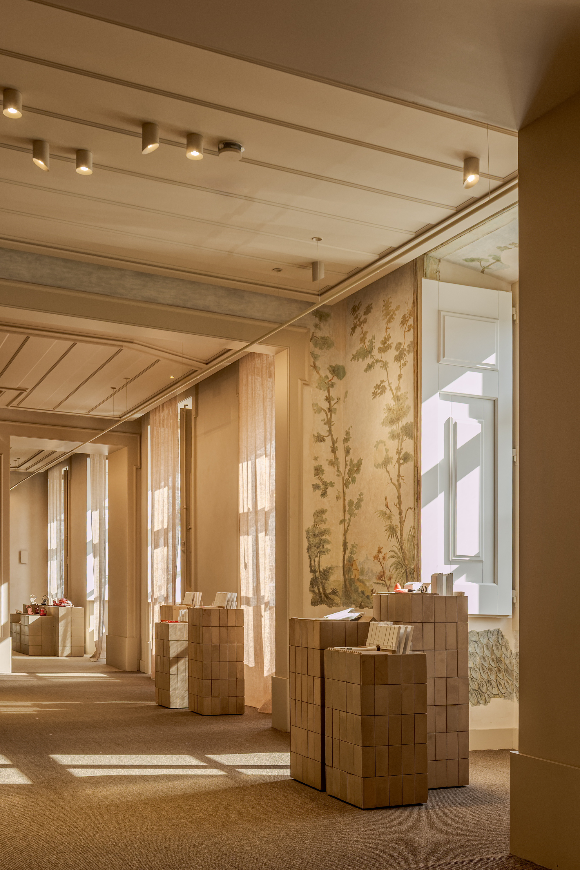 Woven timber display pedestals beneath a botanical mural and slatted wood ceiling near tall windows