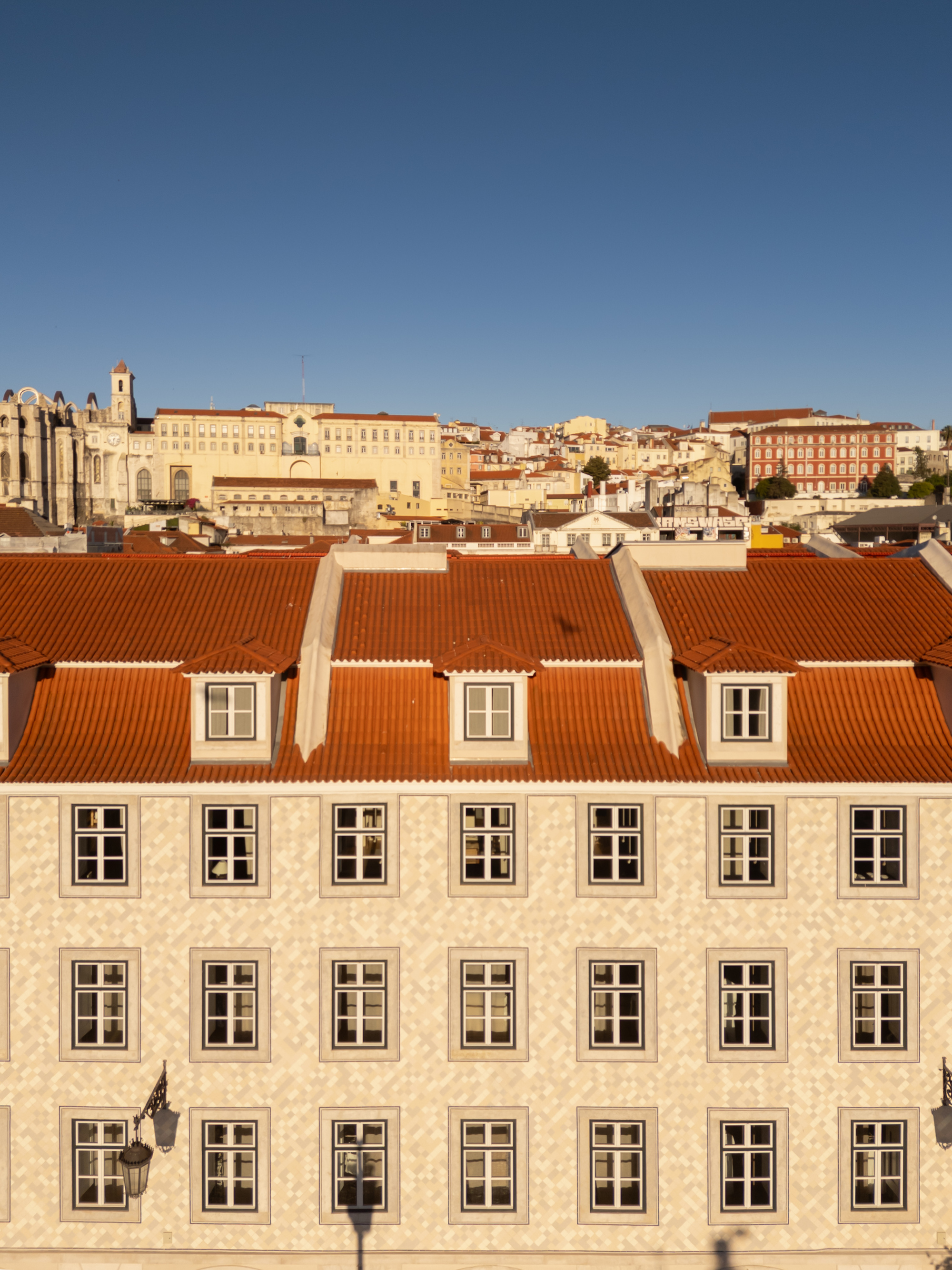 Three-story facade with cream stone cladding and red terra-cotta mansard roof under clear blue sky