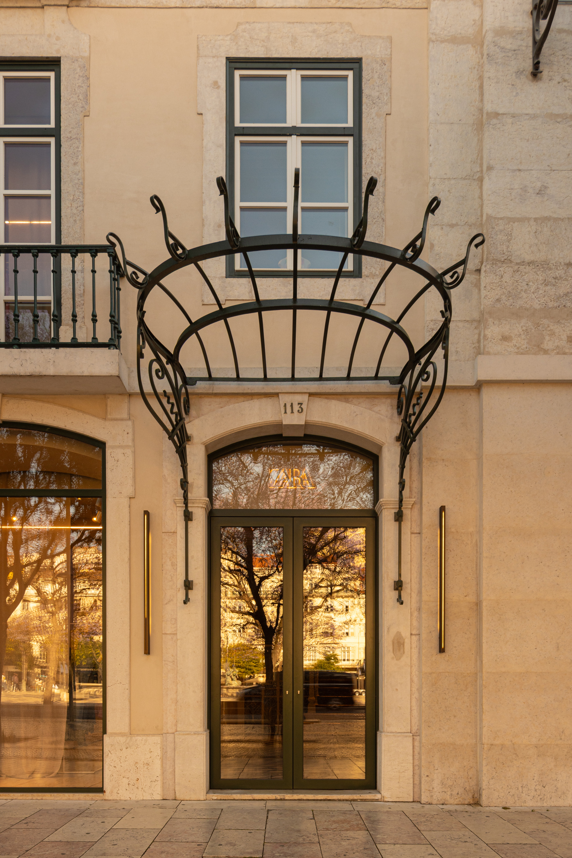 Arched entrance doorway with wrought iron canopy and glass reflecting trees at dusk