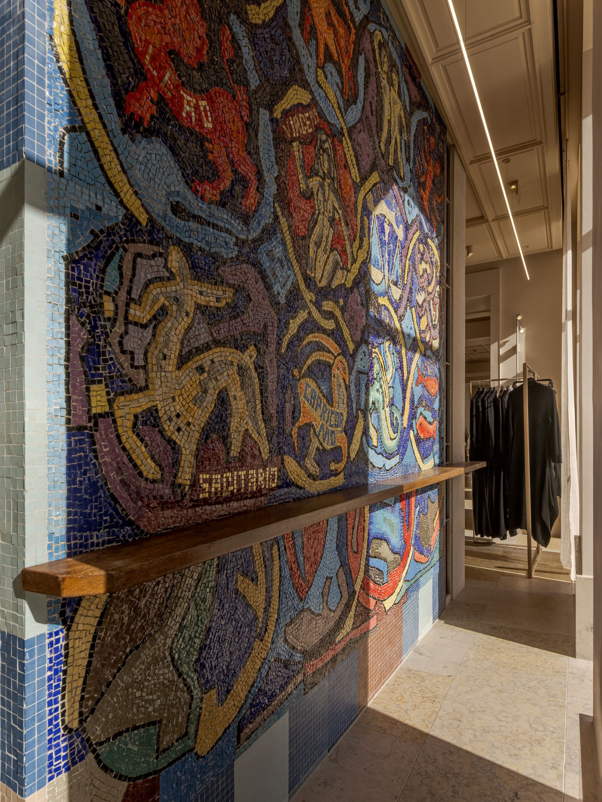 Multicolored glass tile mosaic wall with timber shelf bracket inside a retail corridor with linear lighting