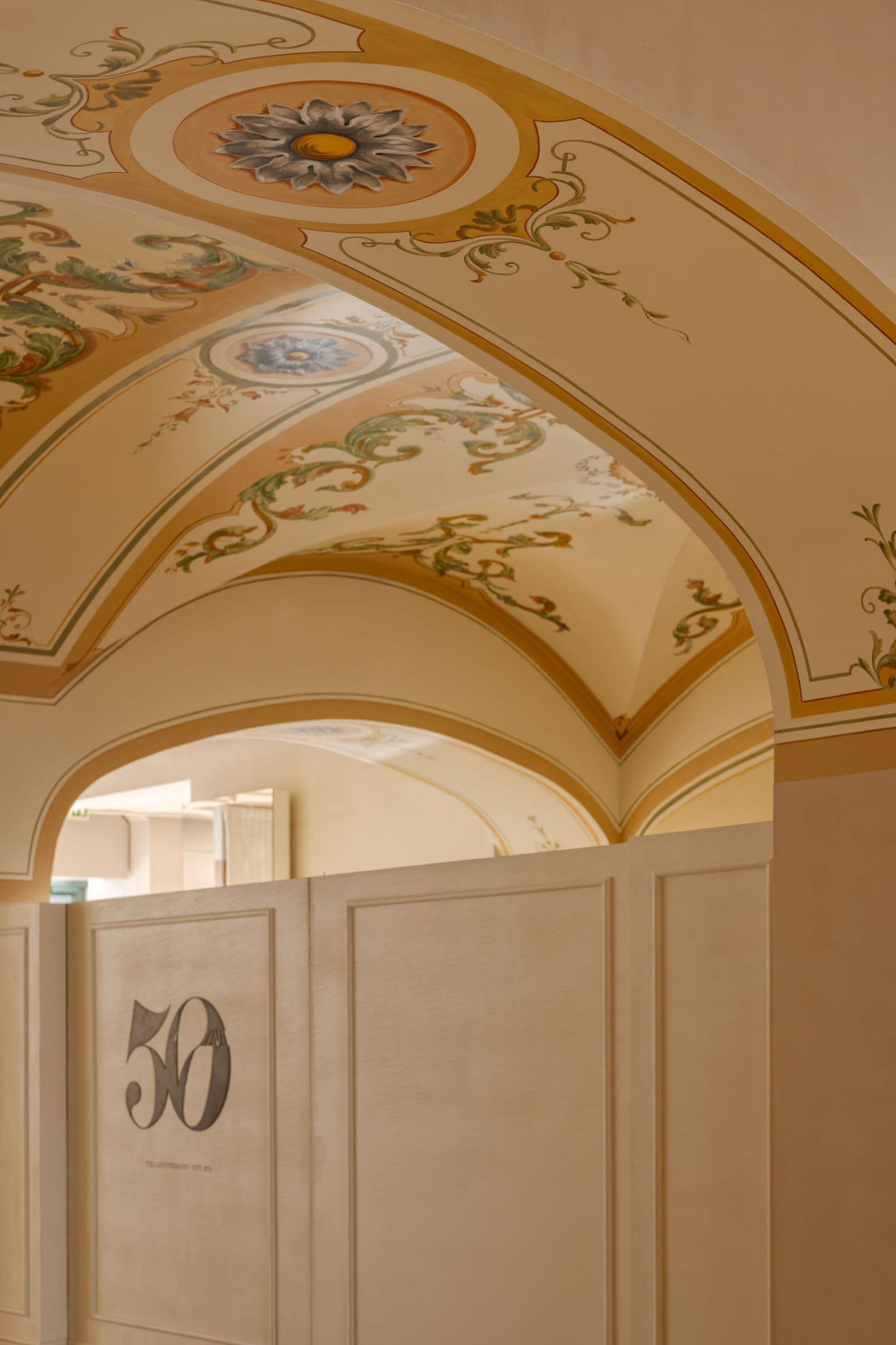 Painted ceiling vault with floral medallions and gilded borders above a paneled wall niche