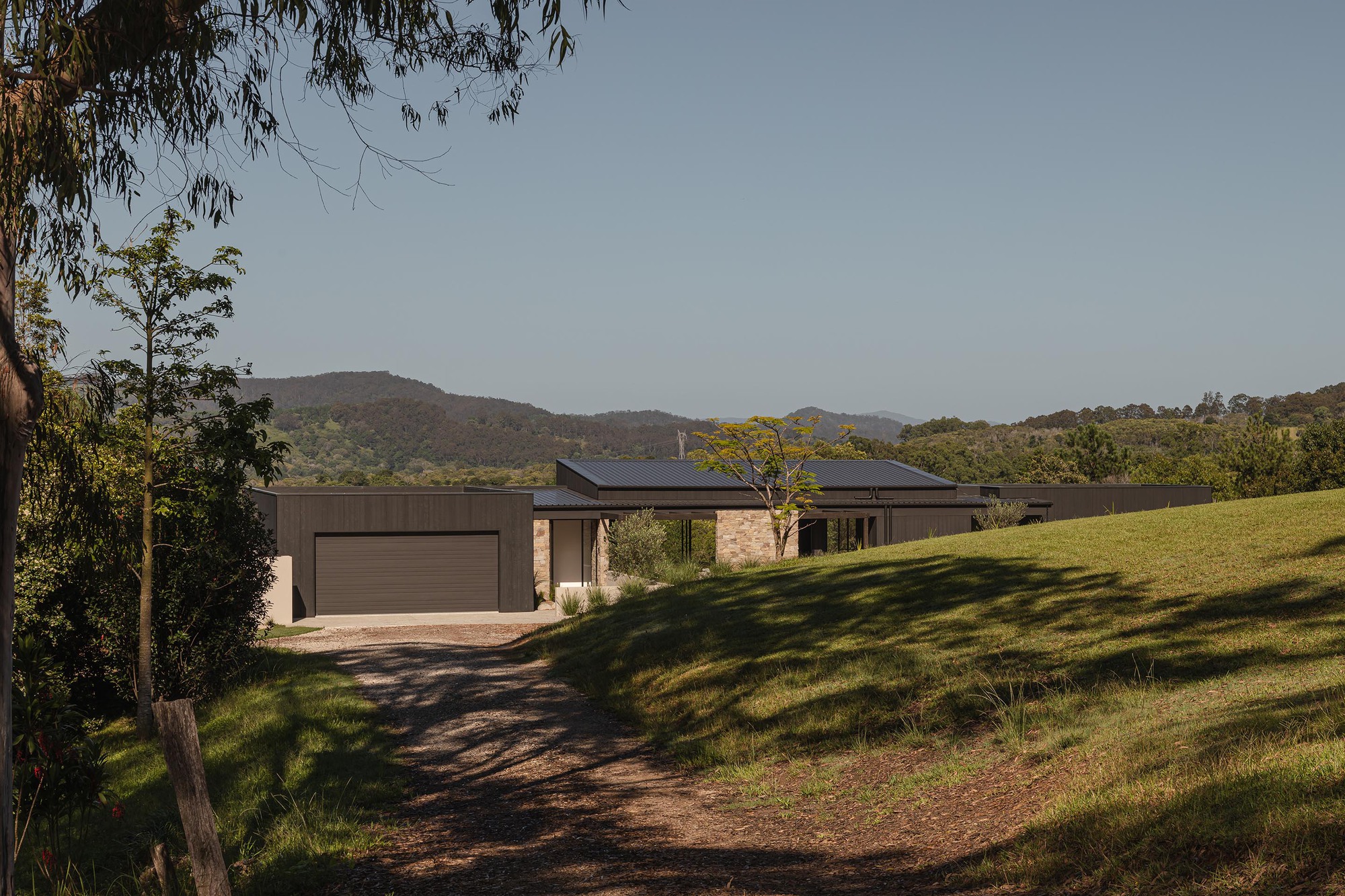 Long view of the horizontal residence nestled on a grassy hillside with eucalyptus trees and distant mountains