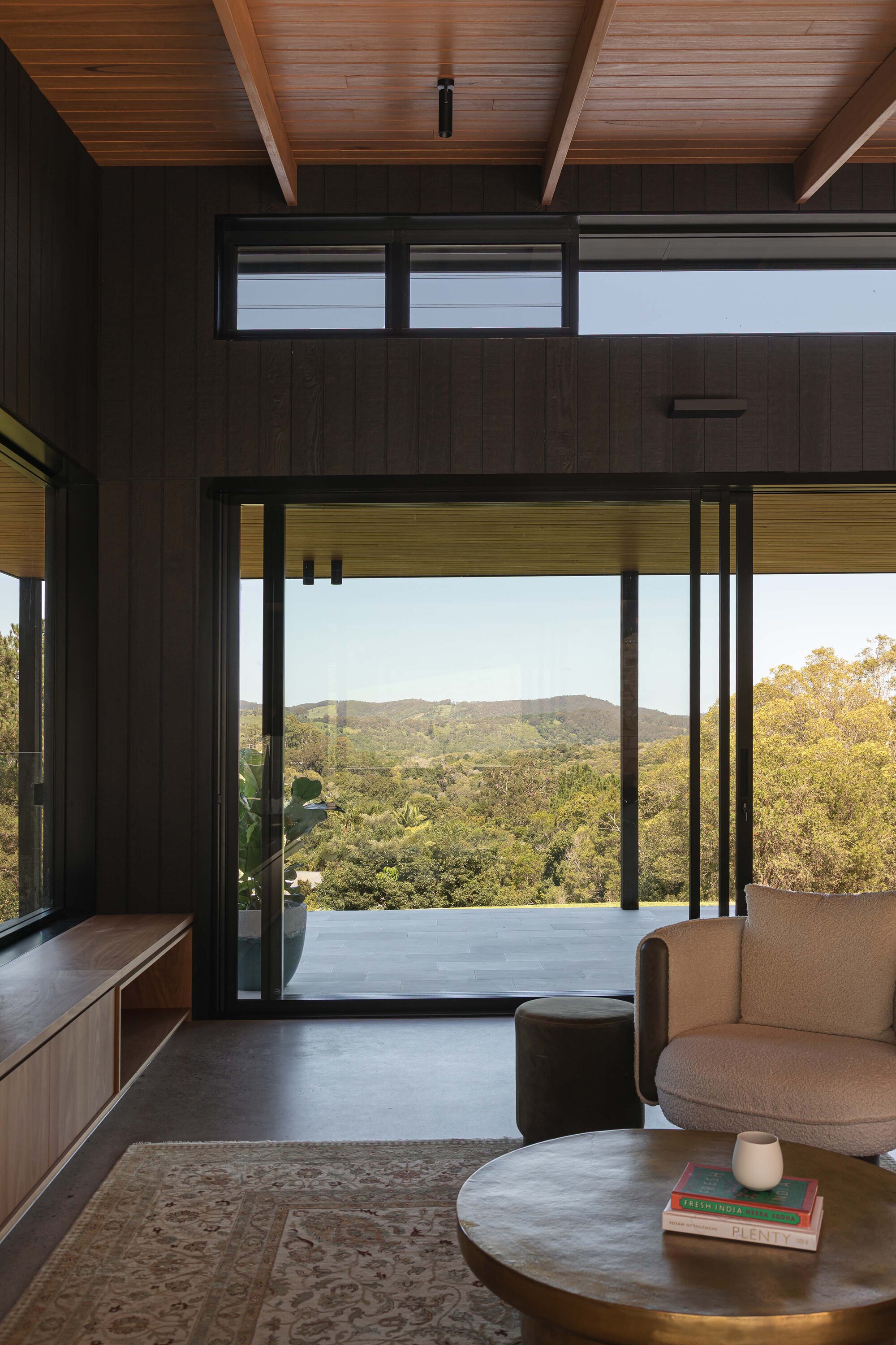 Living room view through glazed doors to the terrace overlooking forested hills under exposed timber rafters