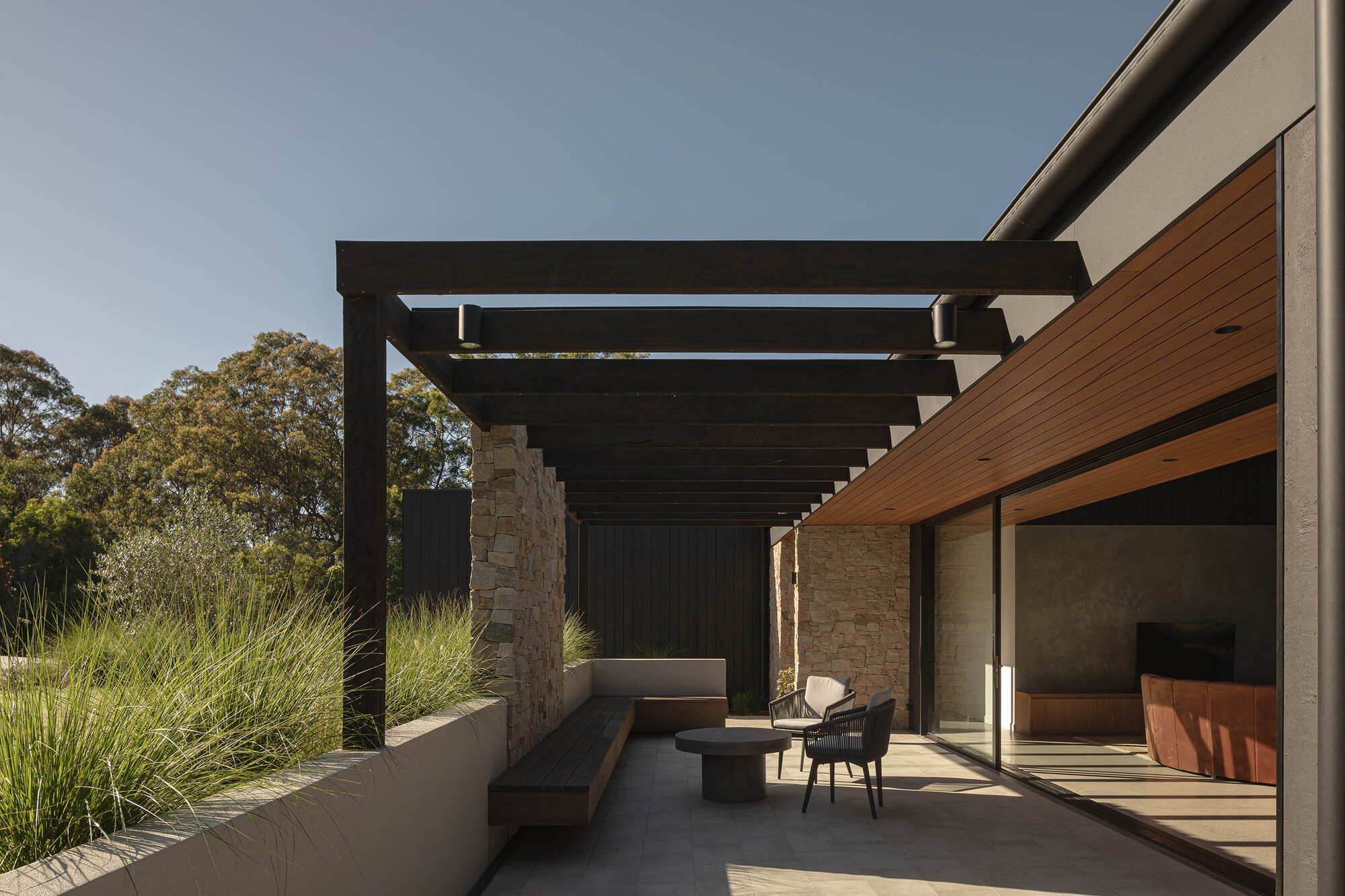Covered terrace with dark timber pergola and stone walls under afternoon sun