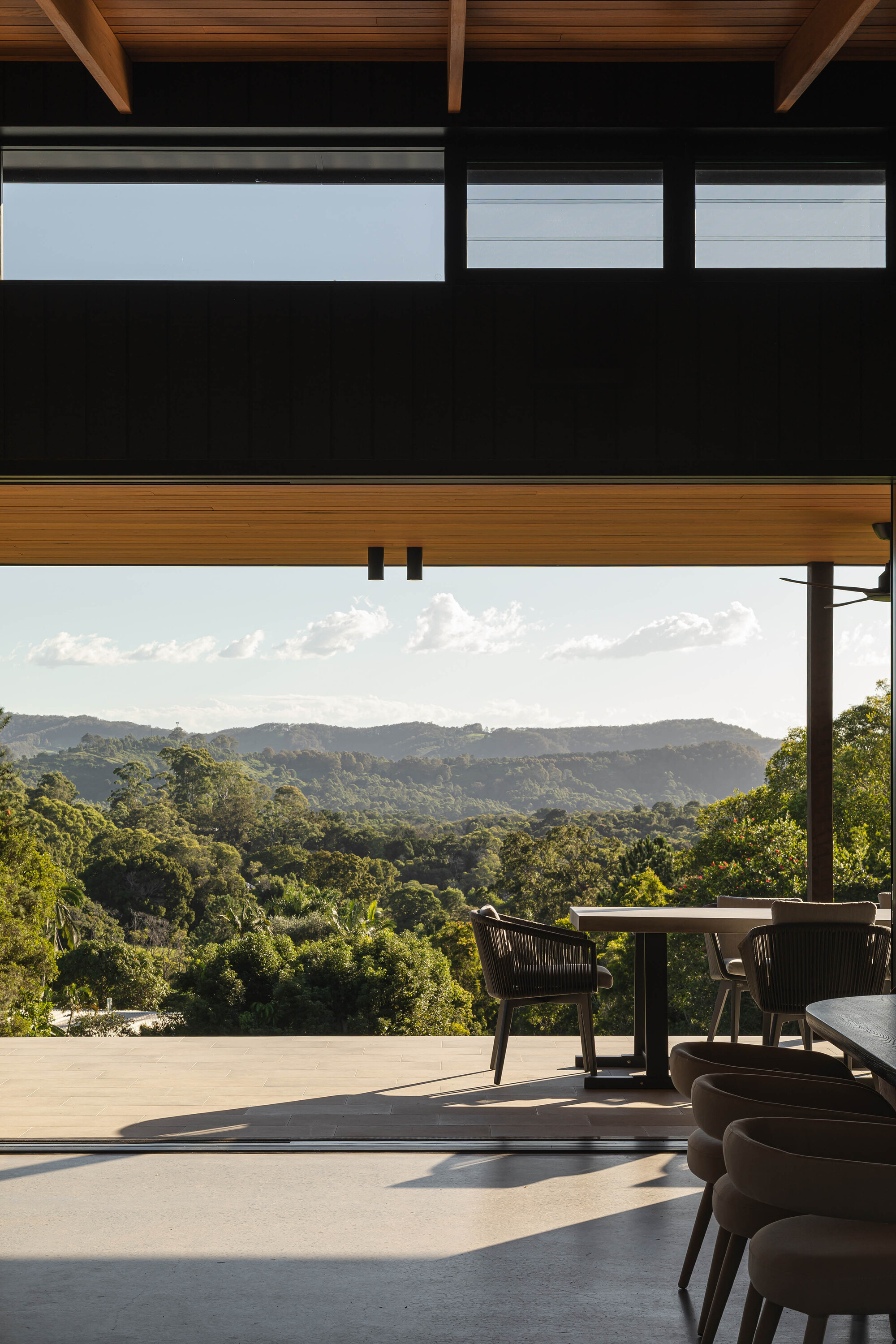 Covered outdoor dining terrace with timber rafters overlooking forested hills at dusk