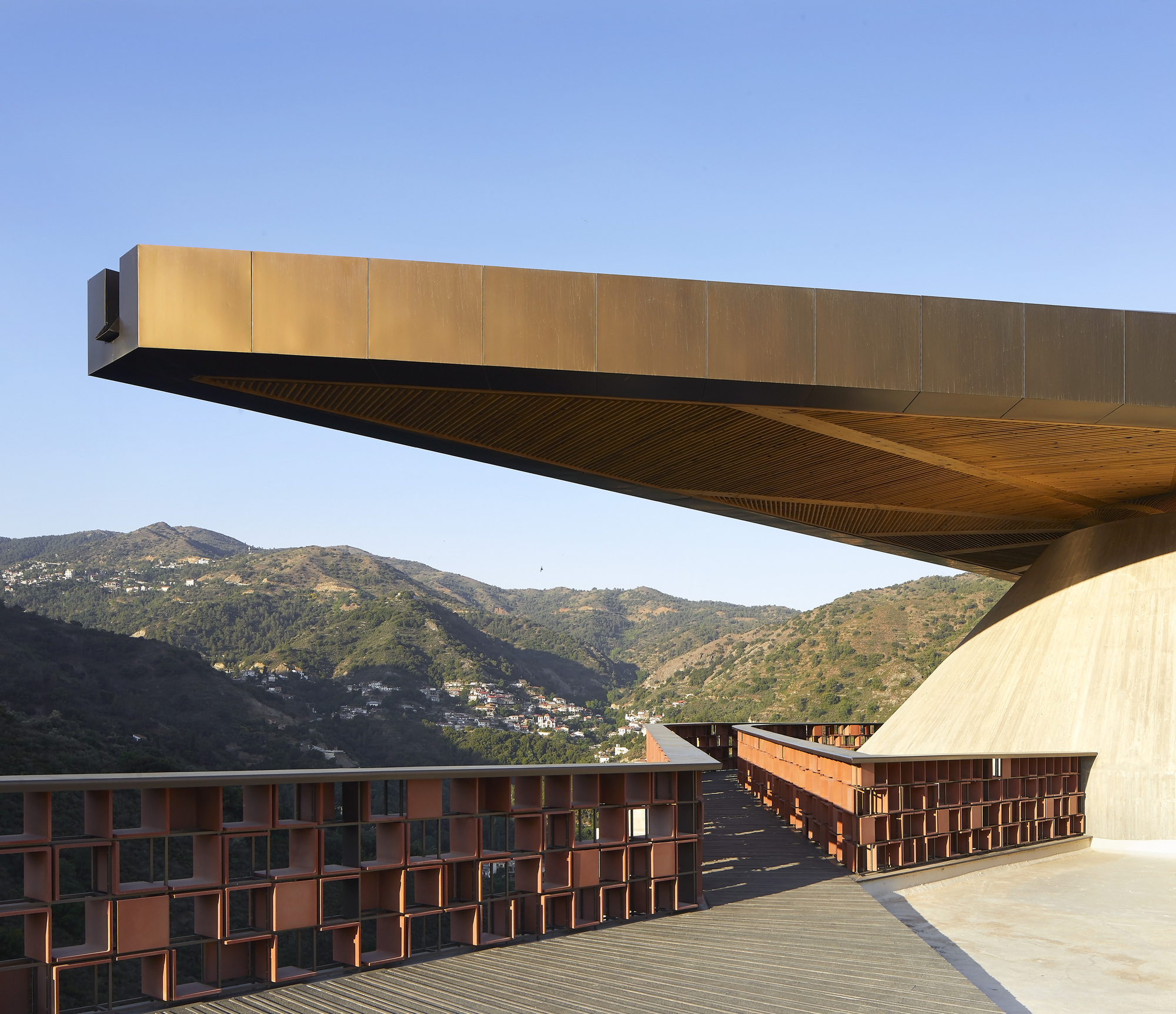 Cantilevered roof overhang with timber soffit above copper-clad volumes and terraced courtyard