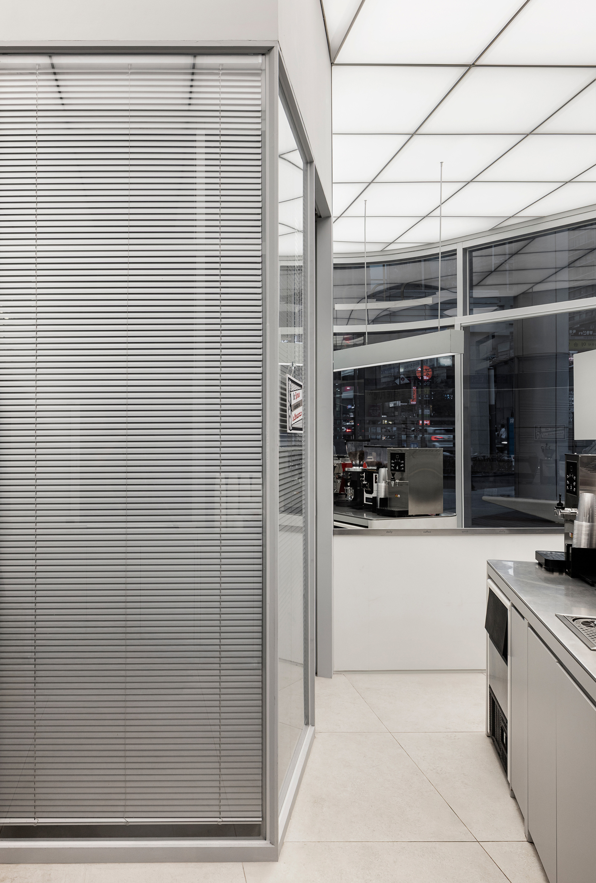 Interior corridor with horizontal metal blinds alongside glass wall under geometric ceiling grid