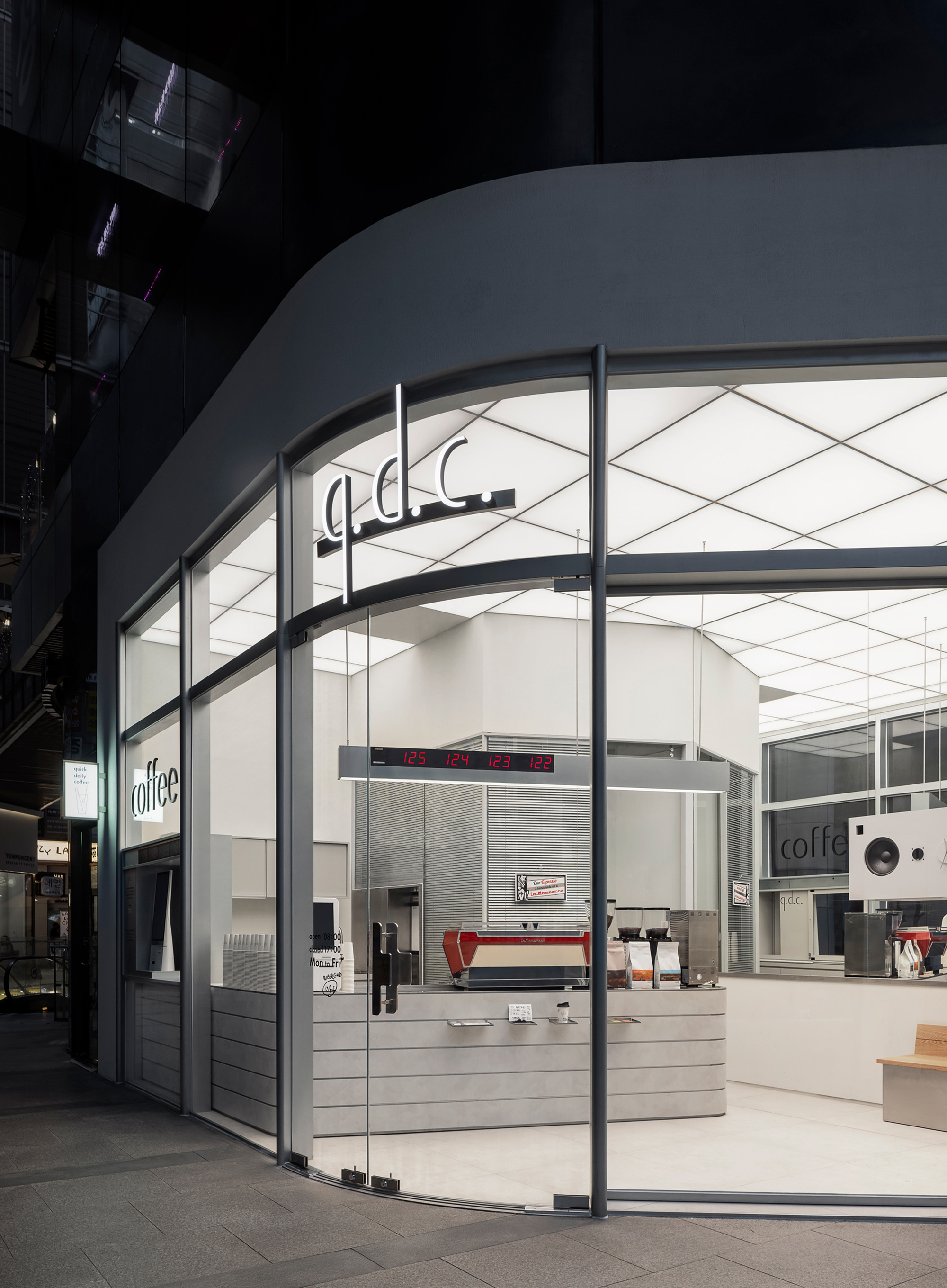 Glass storefront with curved white ceiling and horizontal slatted counter in a shadowed arcade