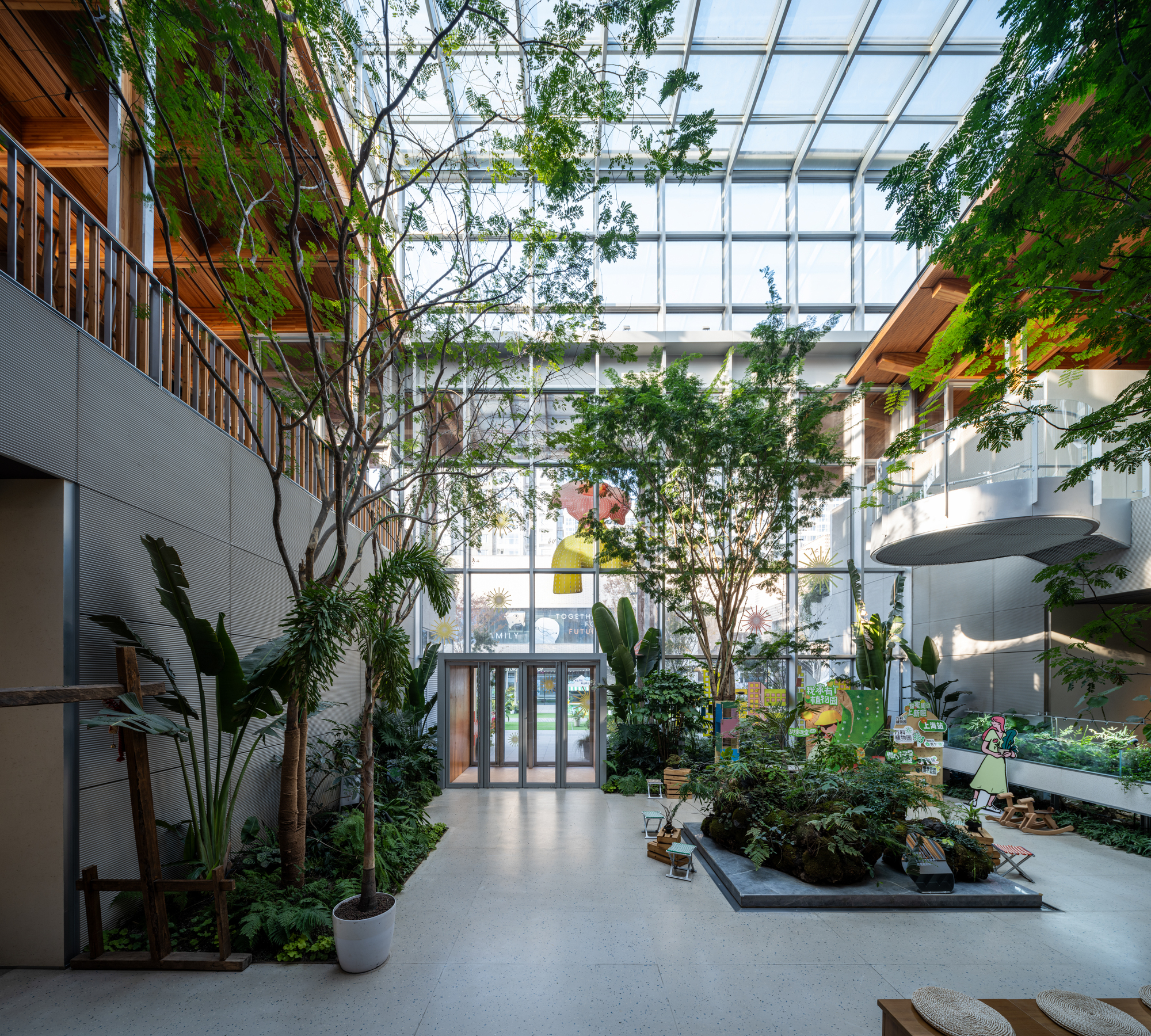 Interior courtyard atrium with full-height glass skylight, mature trees, and planted beds on polished floor