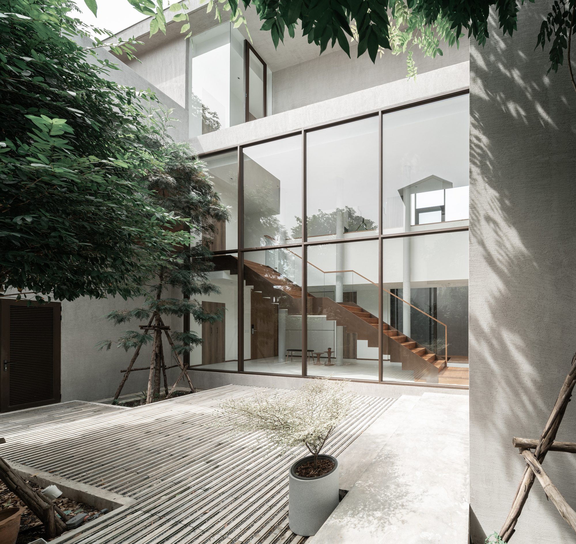Interior courtyard with ribbed concrete ground surface and glazed stairwell framed by planted trees casting shadows