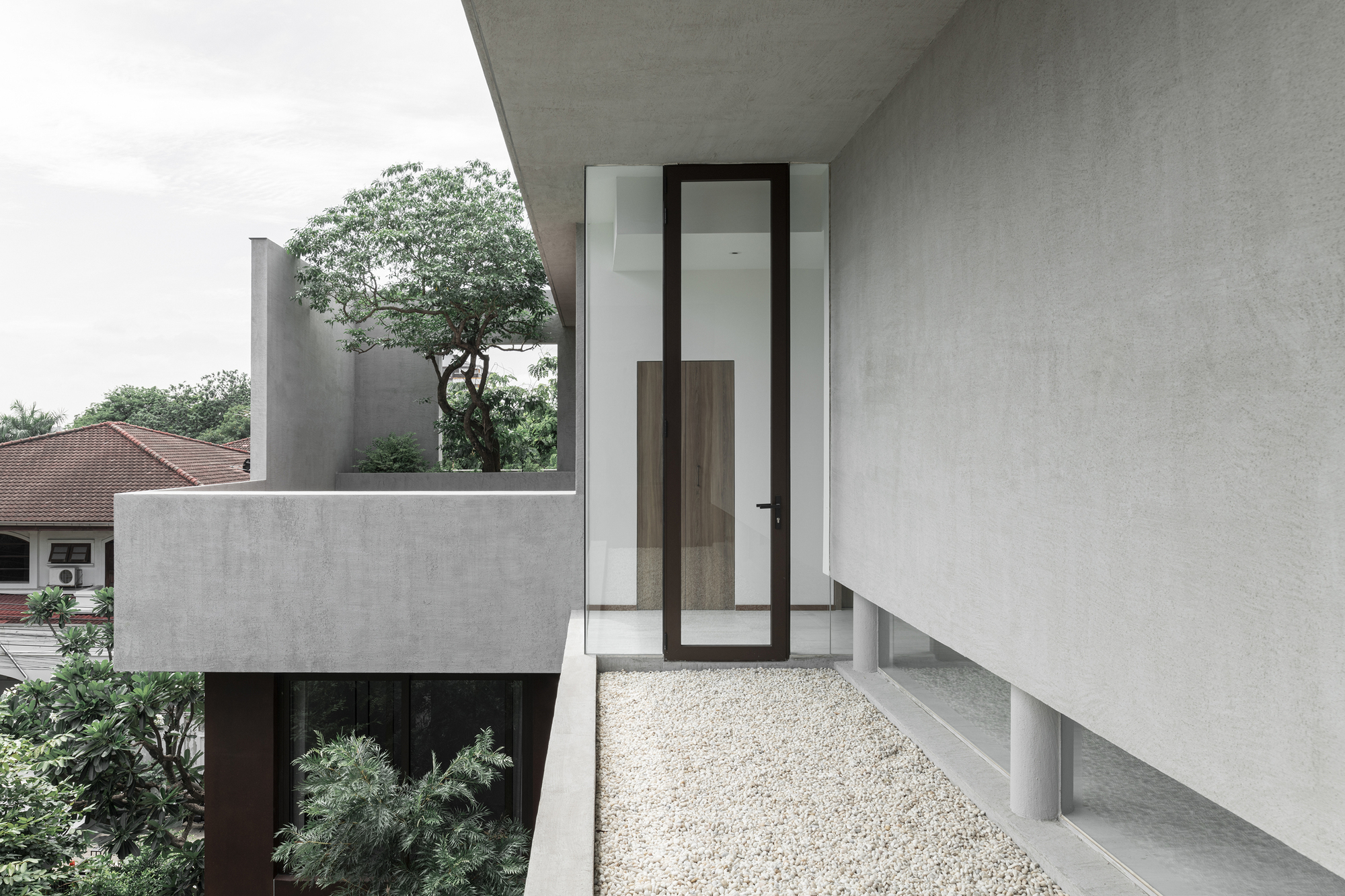 Upper level terrace with gravel flooring and glazed door beneath an angled concrete overhang