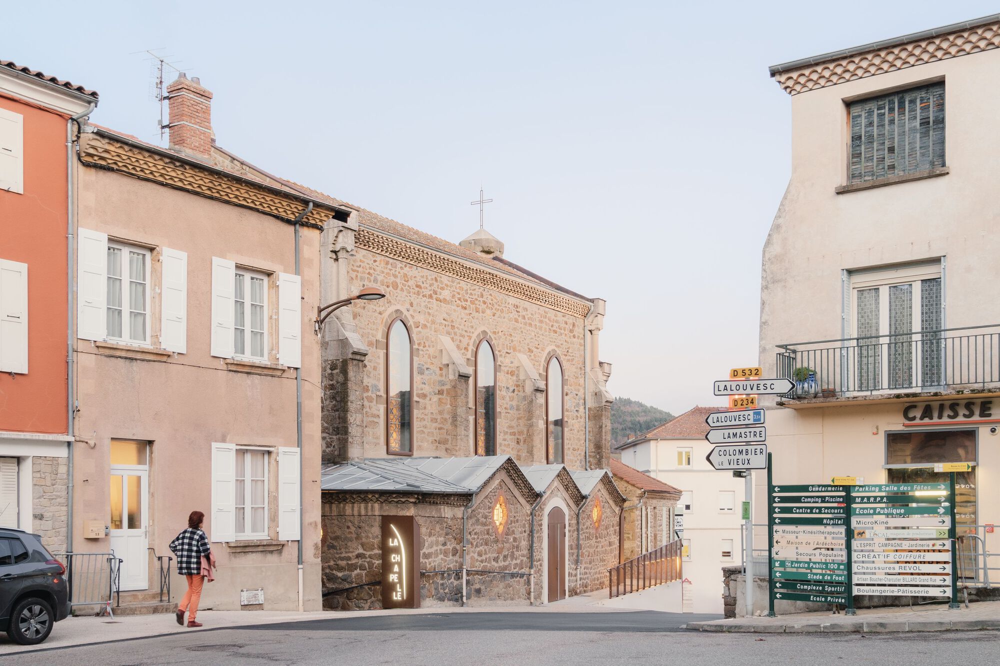 Street view of renovated stone church entrance nestled between residential buildings with person crossing