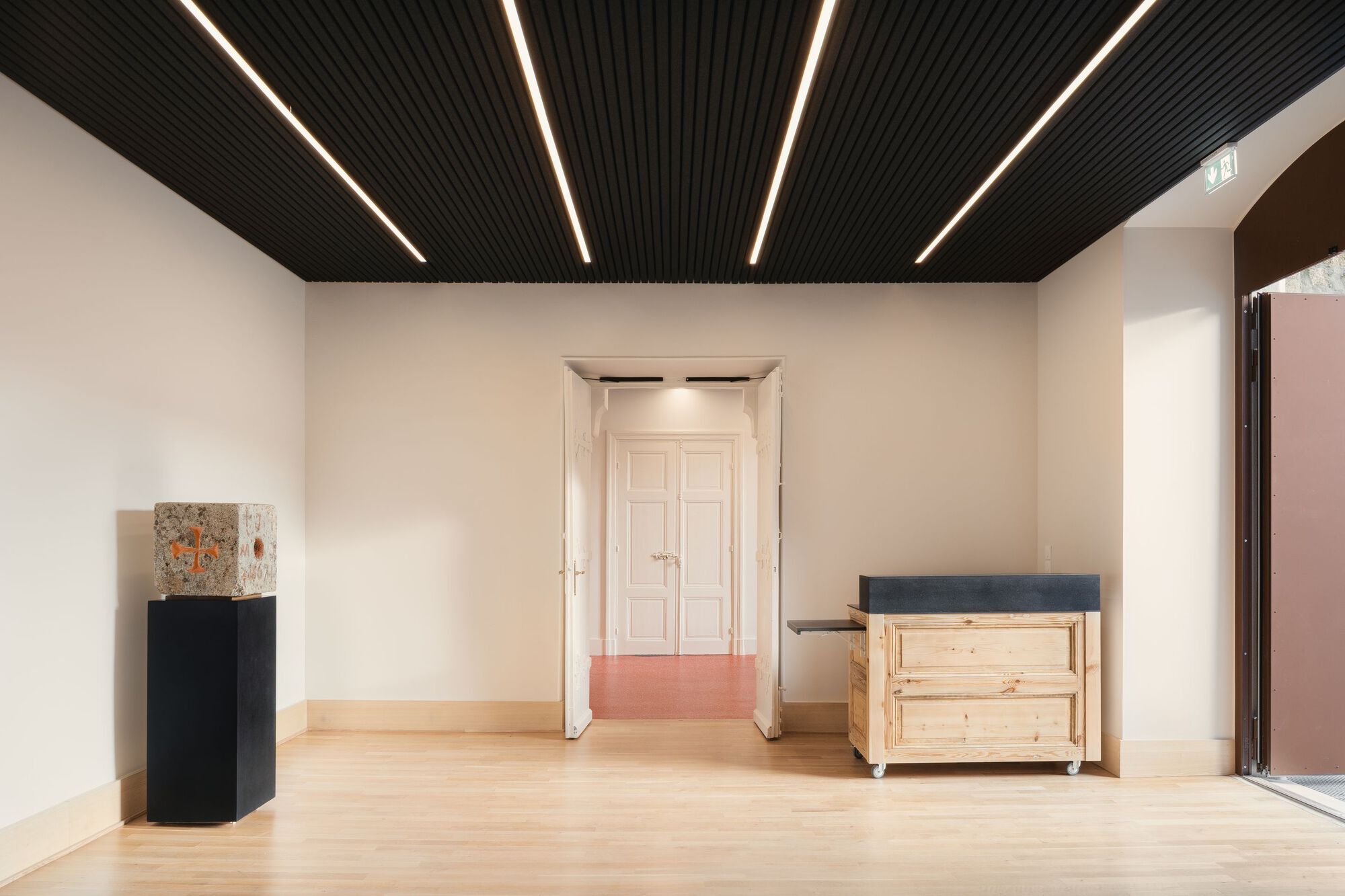 Gallery room with linear black ceiling slats, pale timber floors and white double doors