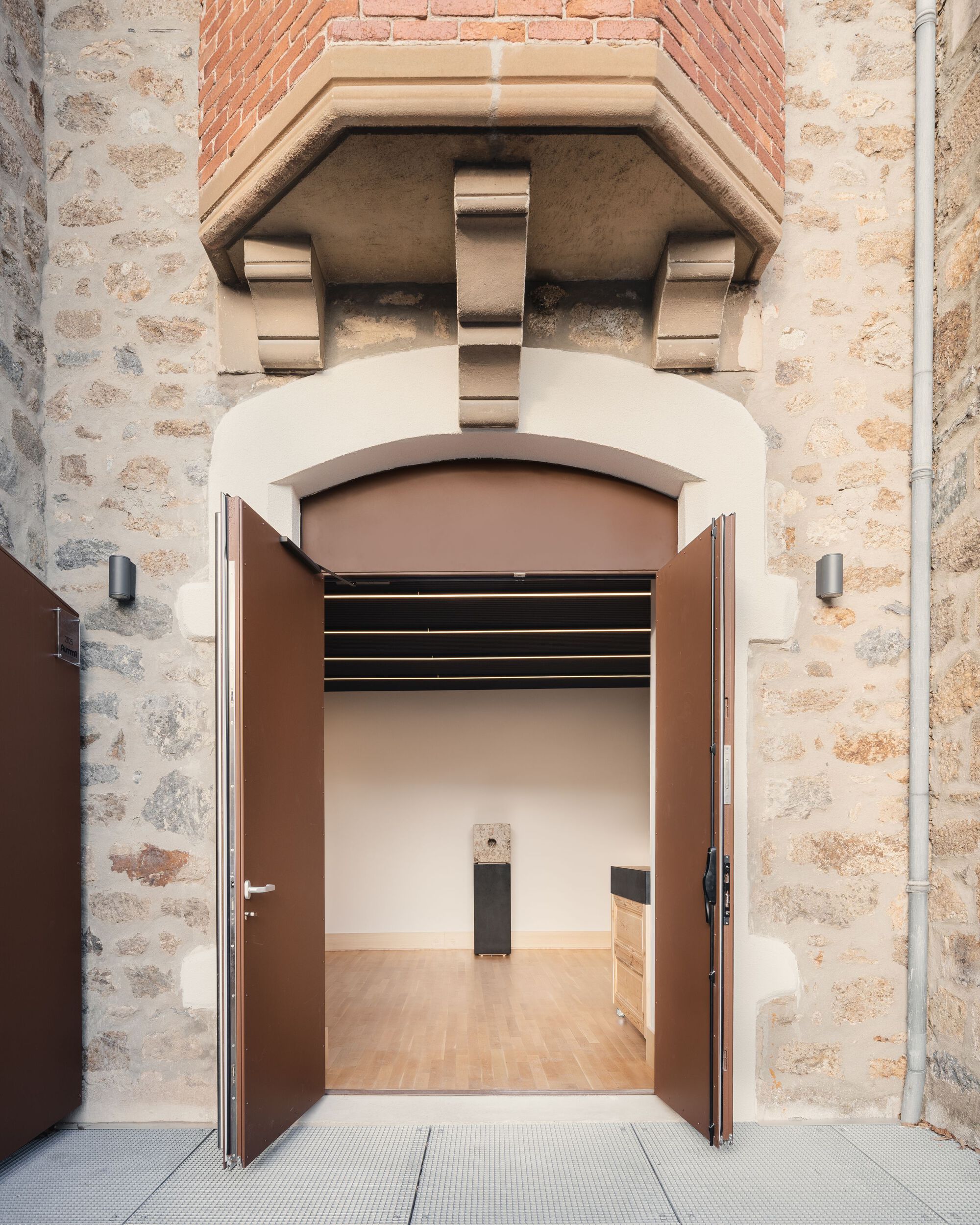 Arched doorway through weathered stone wall leading into a gallery space with timber flooring