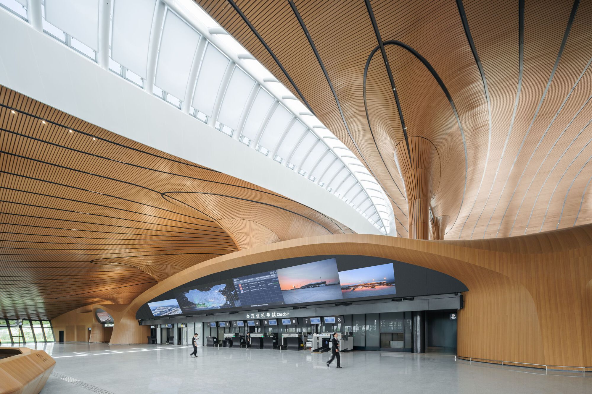 Interior concourse with flowing wood ceiling, a central column, and passengers near the ticket counters