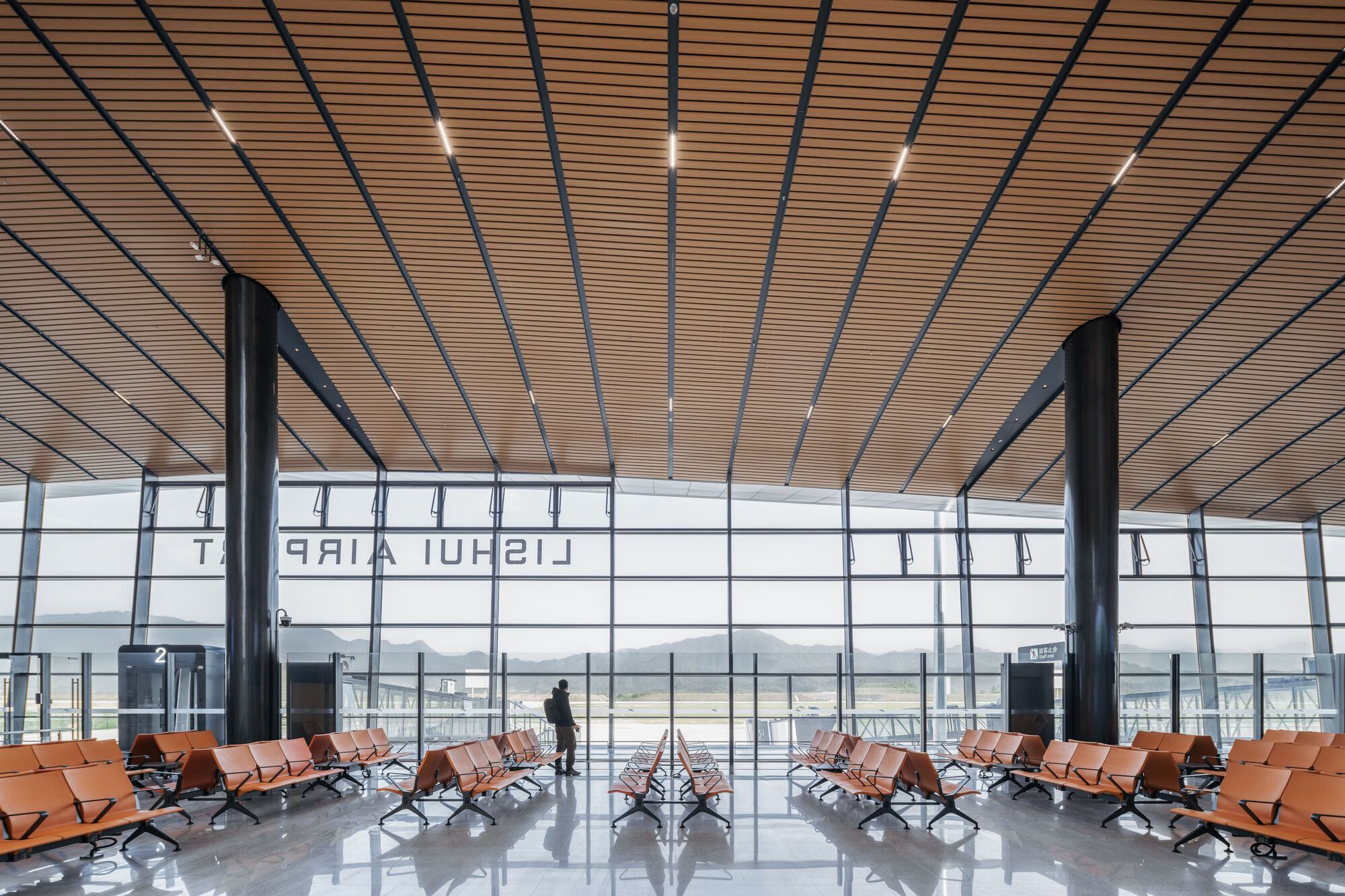 Departure gate seating area with wood-slat ceiling and floor-to-ceiling glazing overlooking the airfield