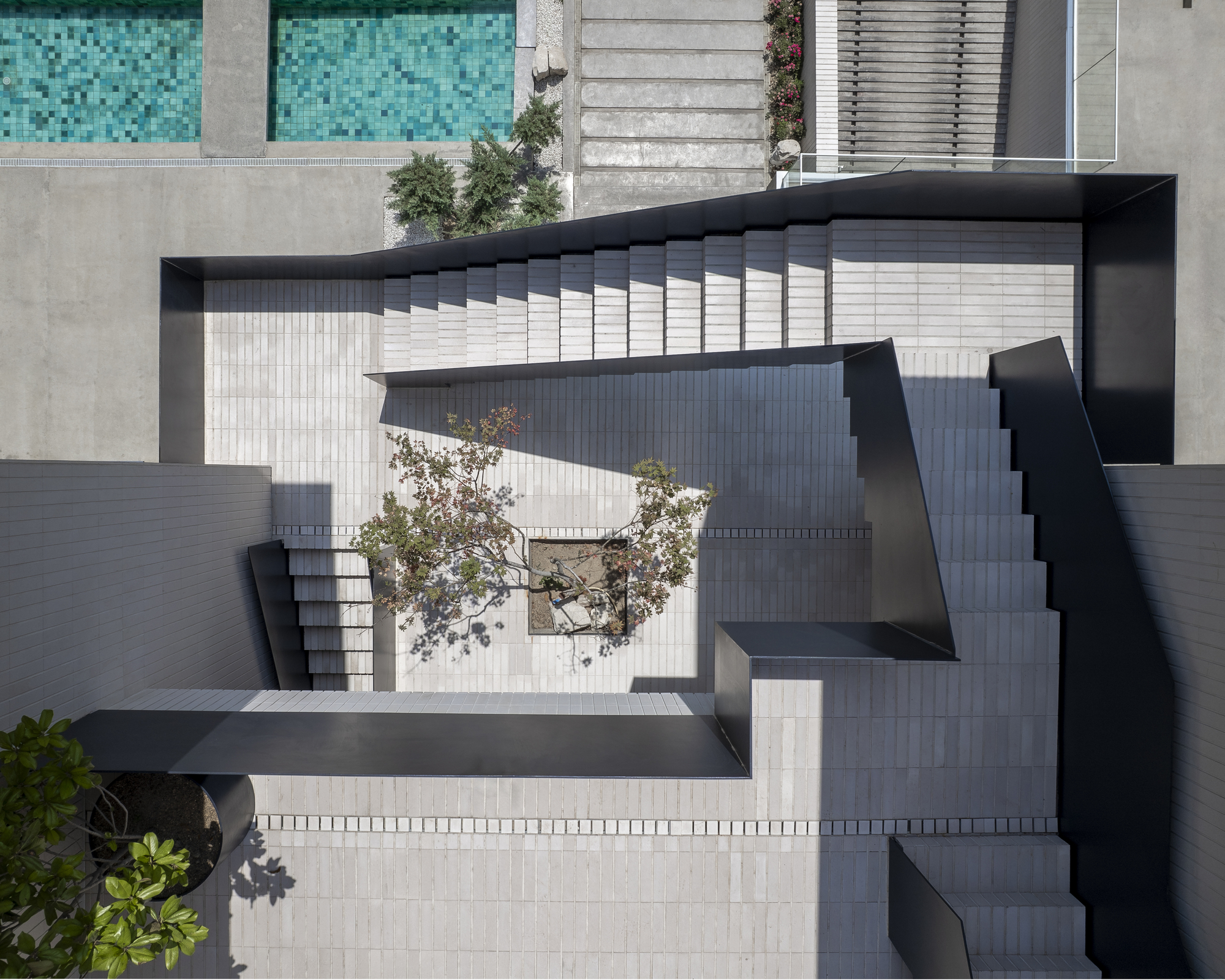 Top-down view of the zigzagging black staircase connecting multiple terrace levels with small planted trees below