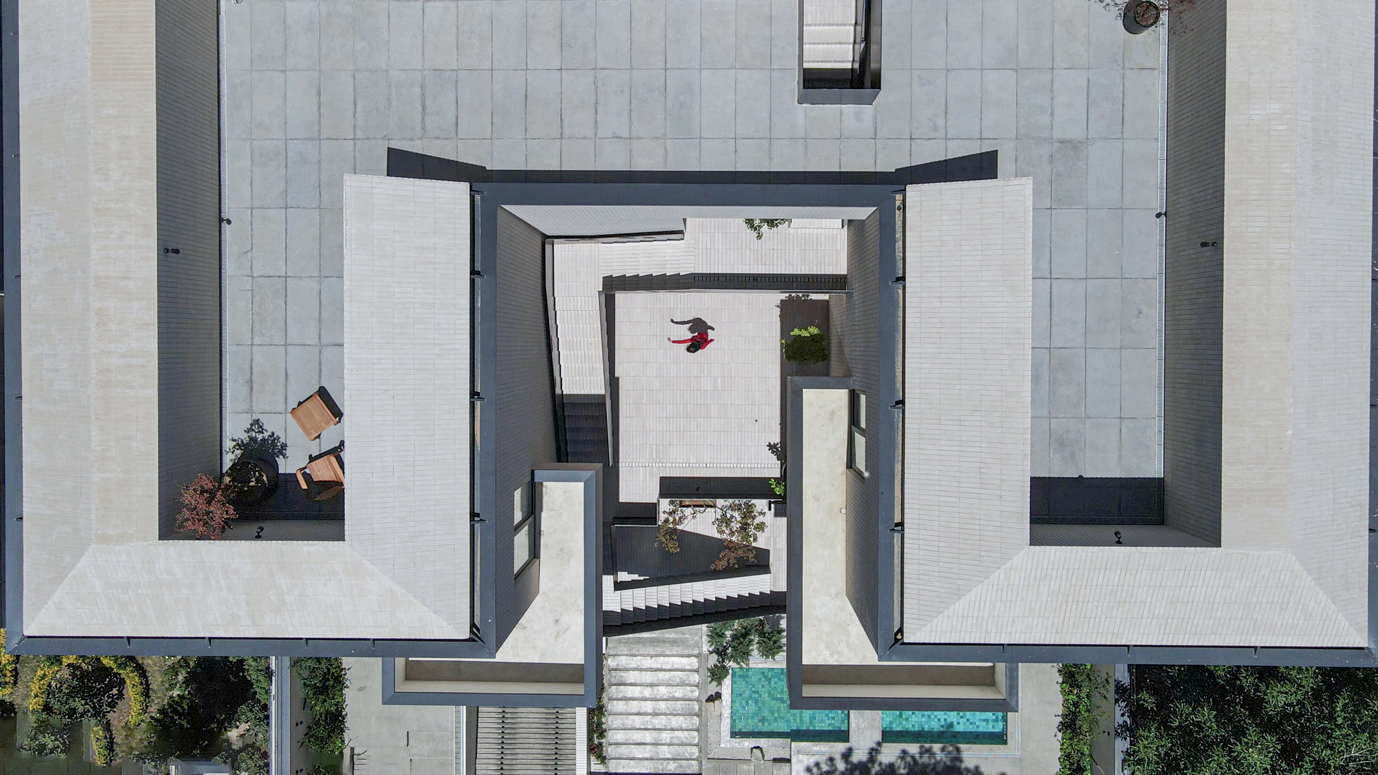 Overhead view of central stairwell with white stone paving, black metal stair volumes and turquoise pool edges