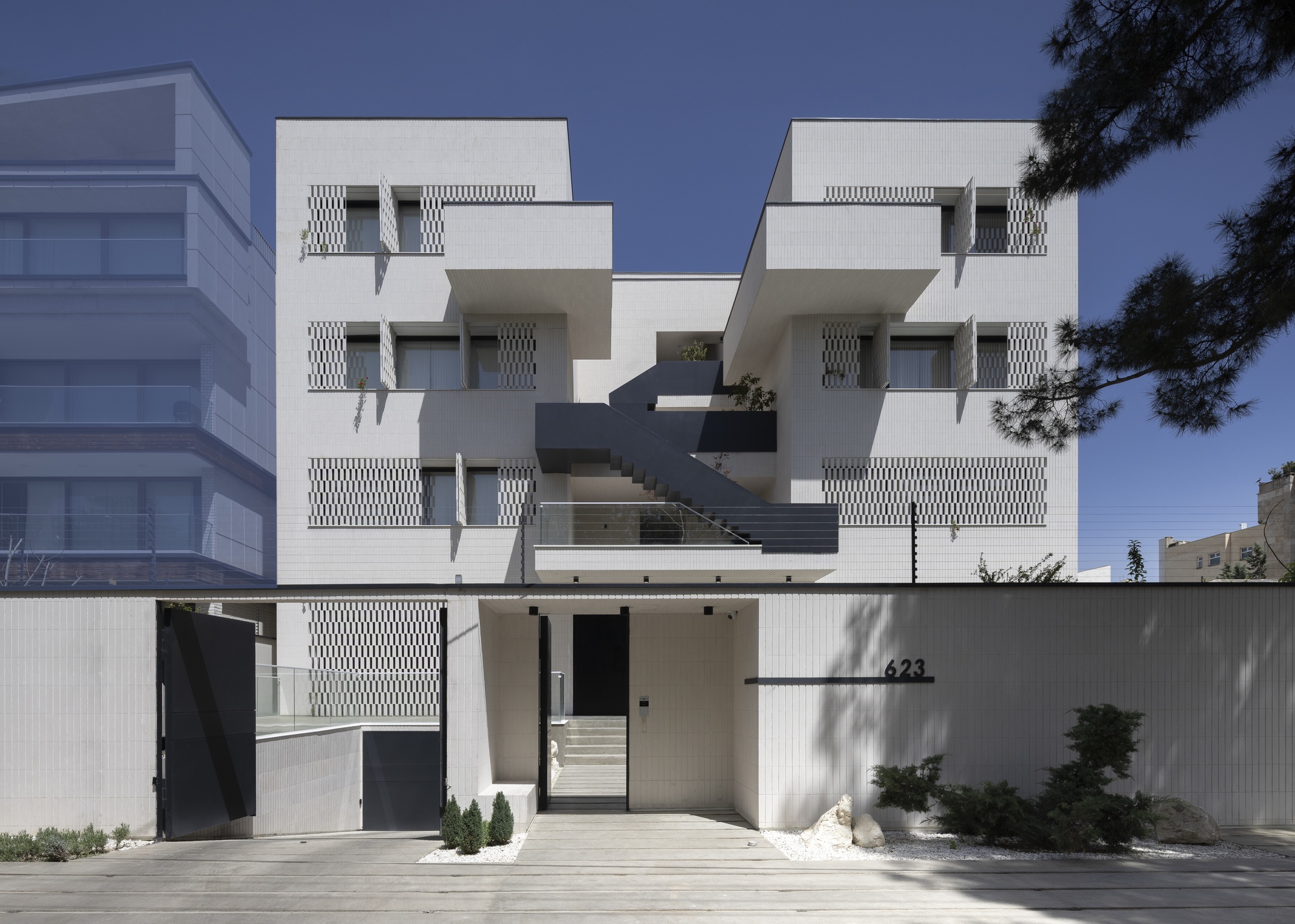 Frontal view of the symmetrical apartment block showing repeating perforated panels and projecting planters under blue sky