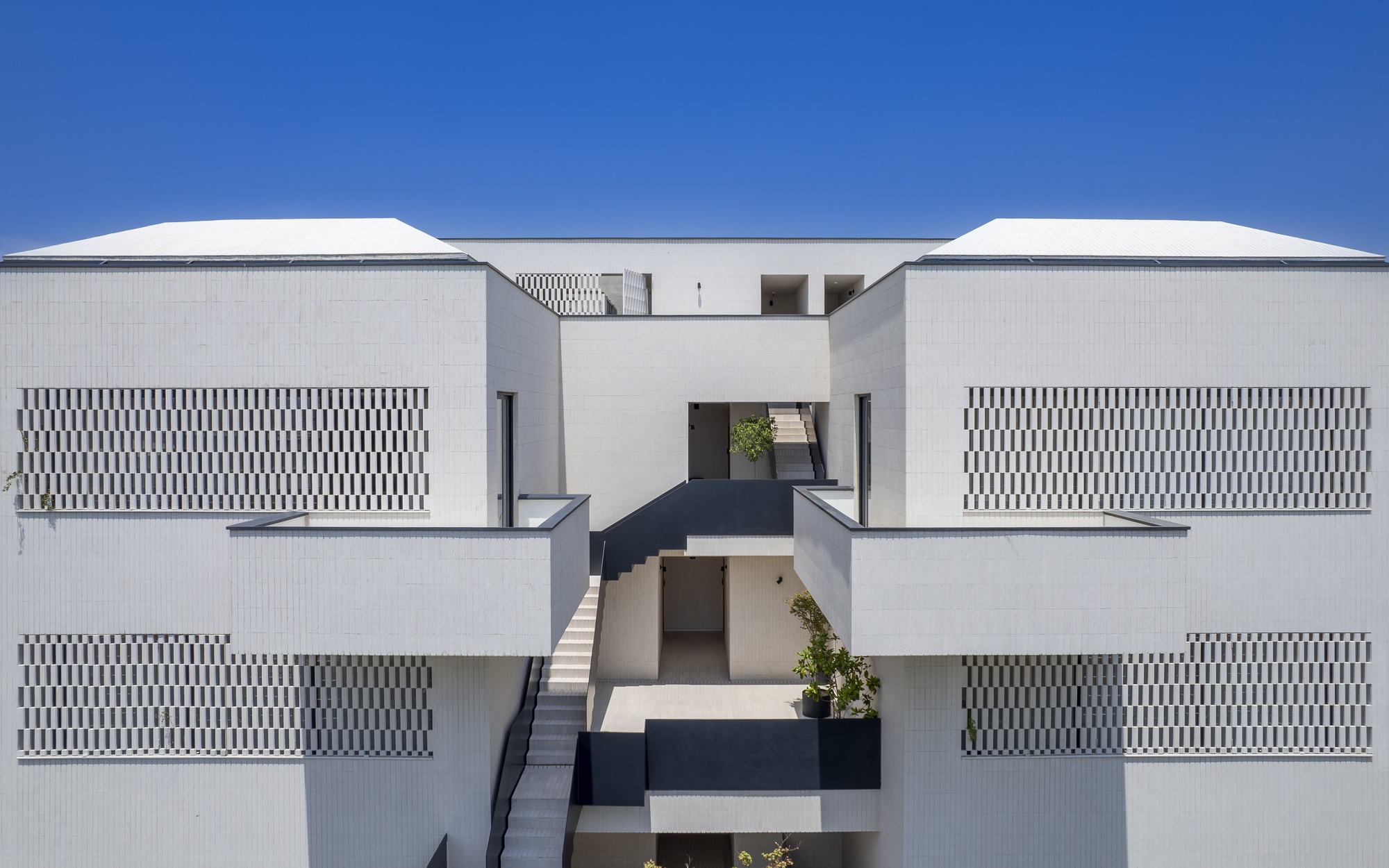 Head-on view of the central void with suspended bridges and geometric balcony screens under bright sunlight