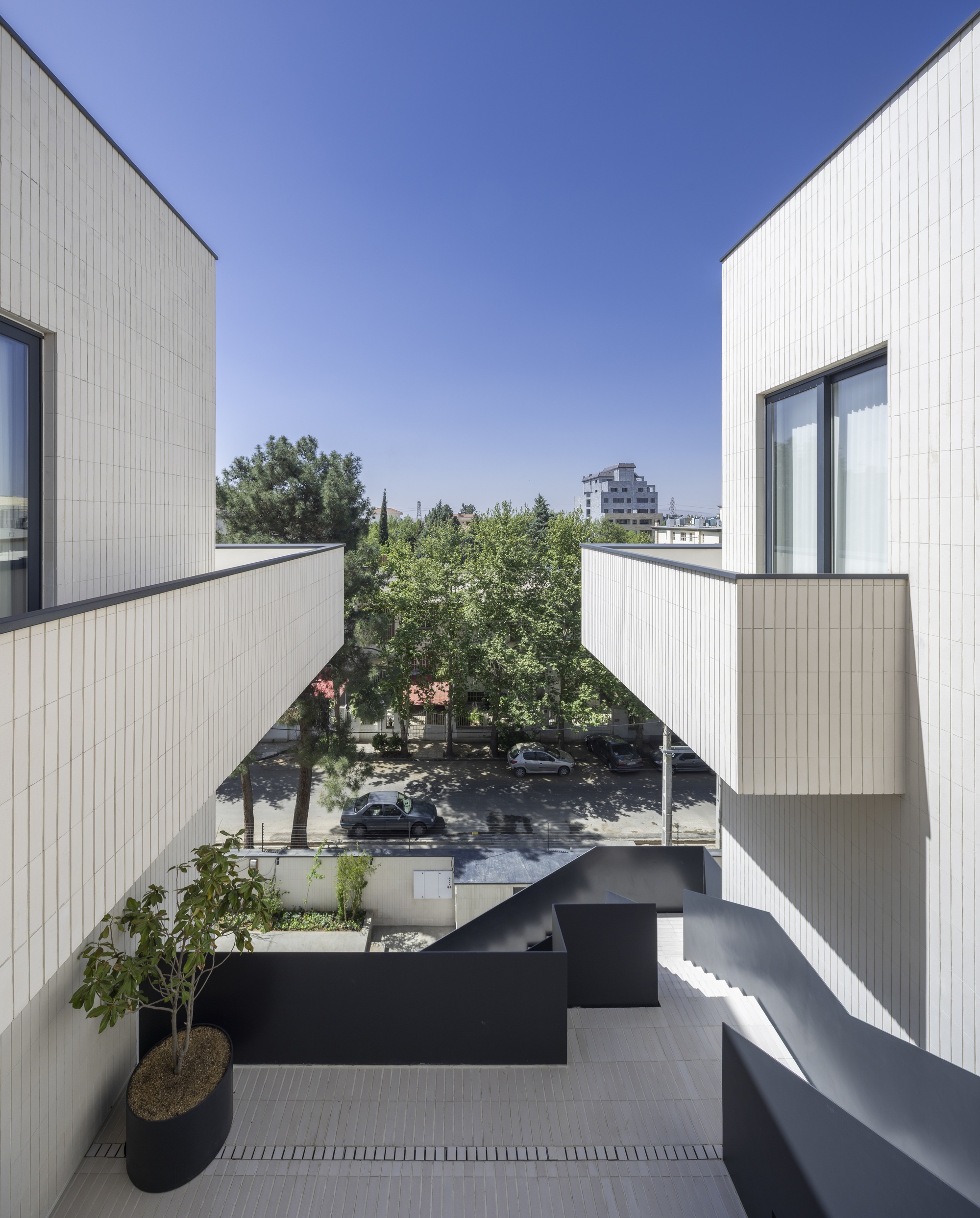 Rooftop terrace with cantilevered black steel walkways and white corrugated cladding overlooking a tree-lined street