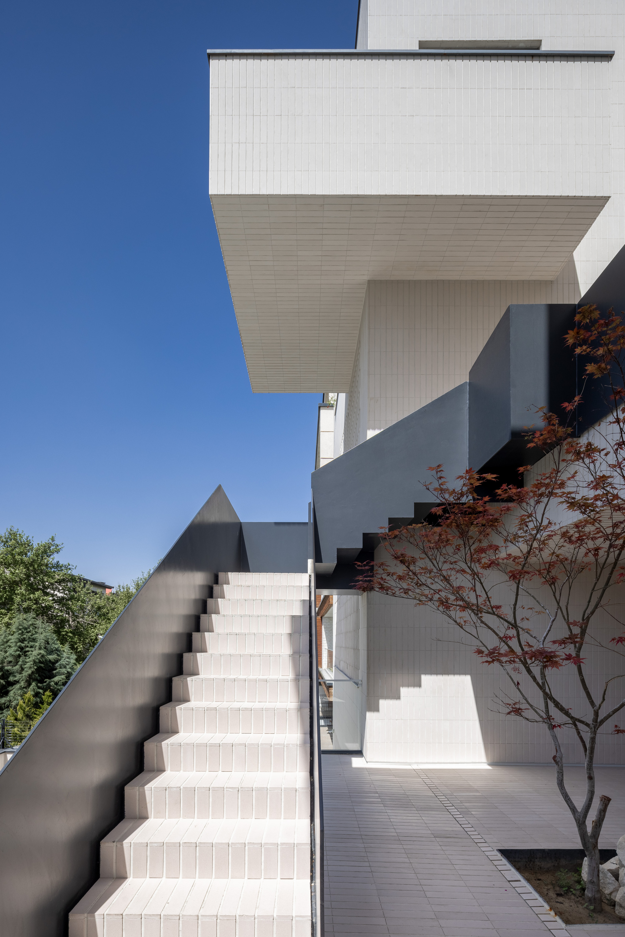Exterior staircase with white tiled risers and dark metal handrail ascending between cantilevered volumes