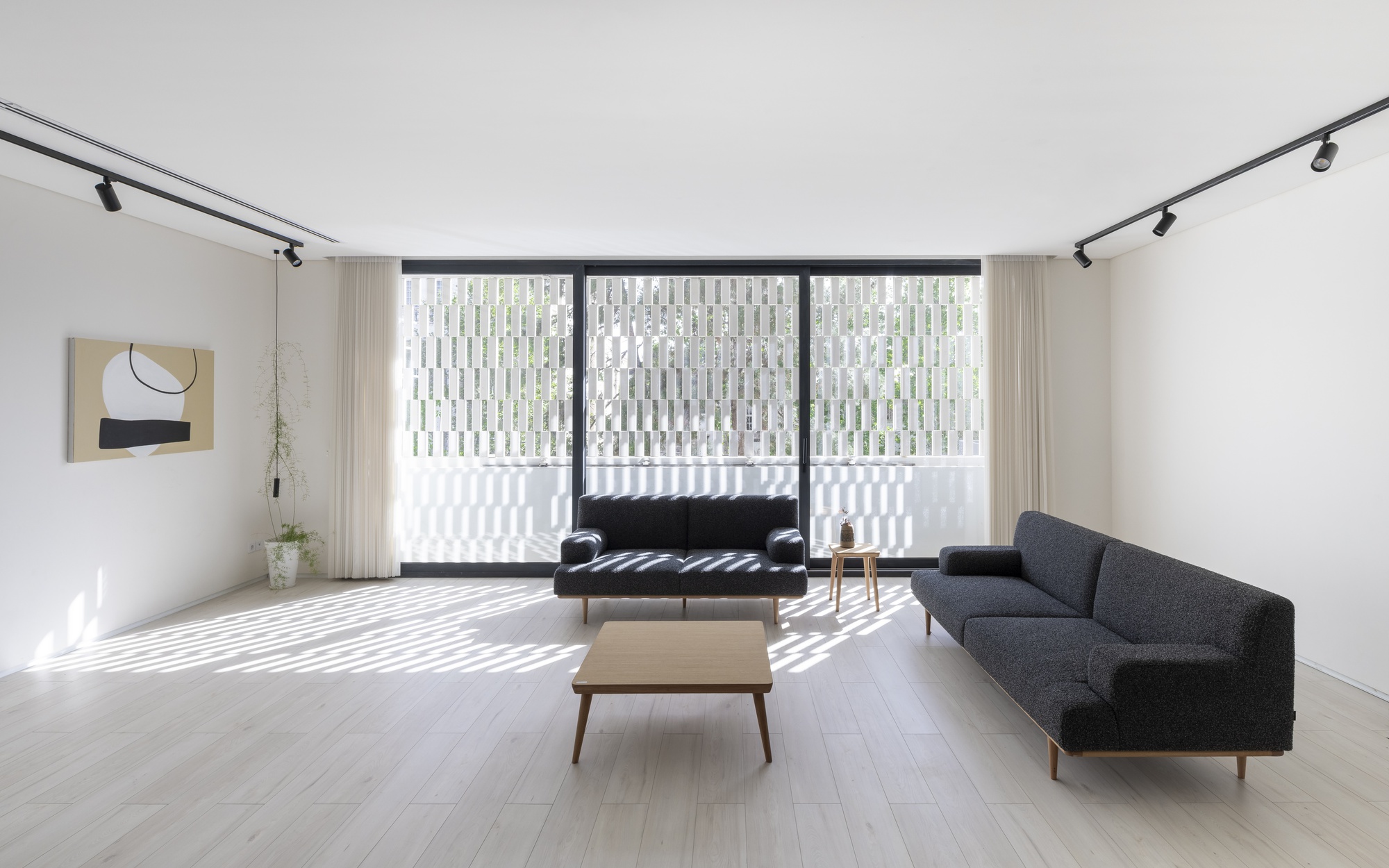 Living room with light wood flooring and striped shadow patterns from vertical screen beyond glazing