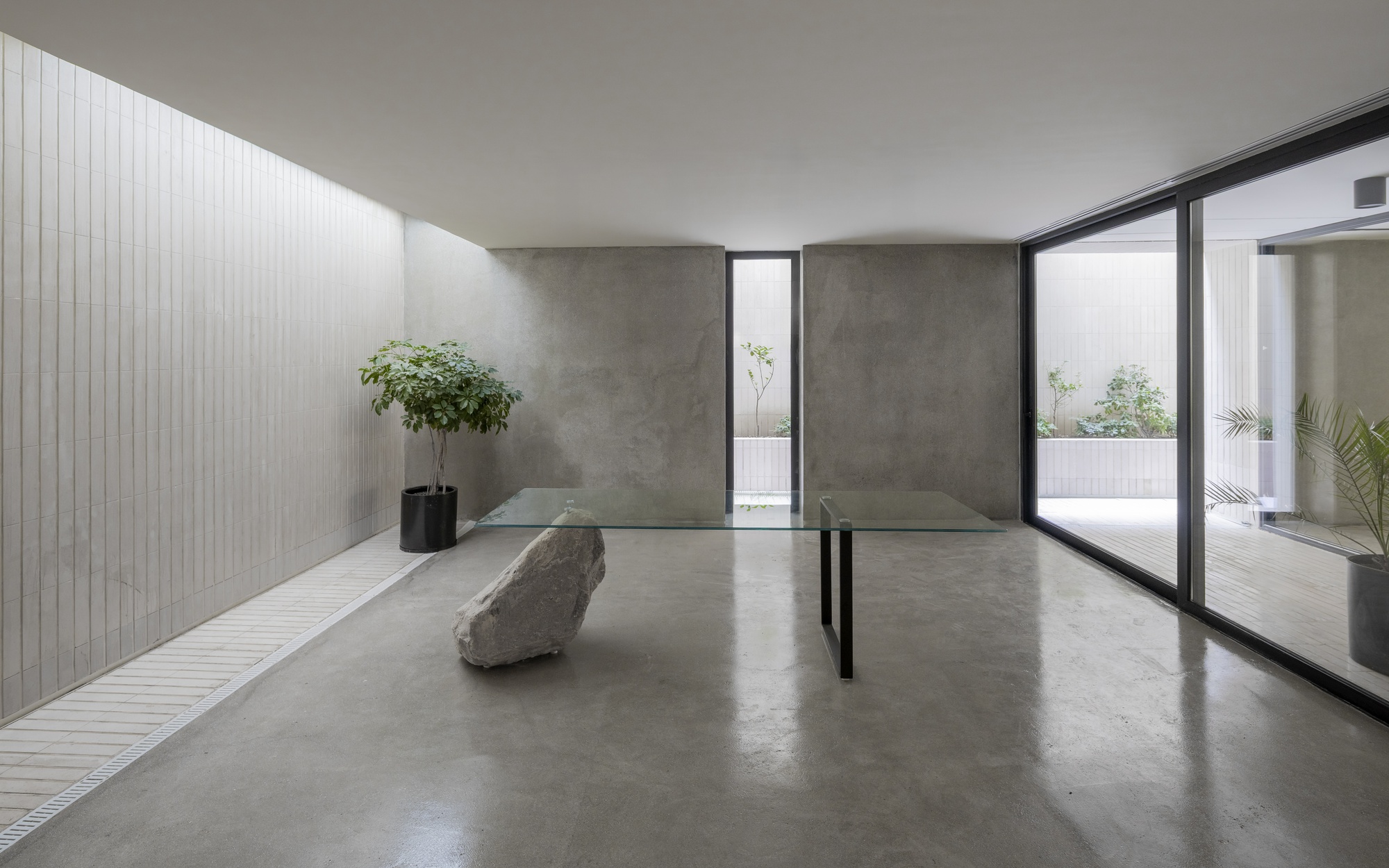 Polished concrete floor gallery with raw stone sculpture and glass doors opening to terrace