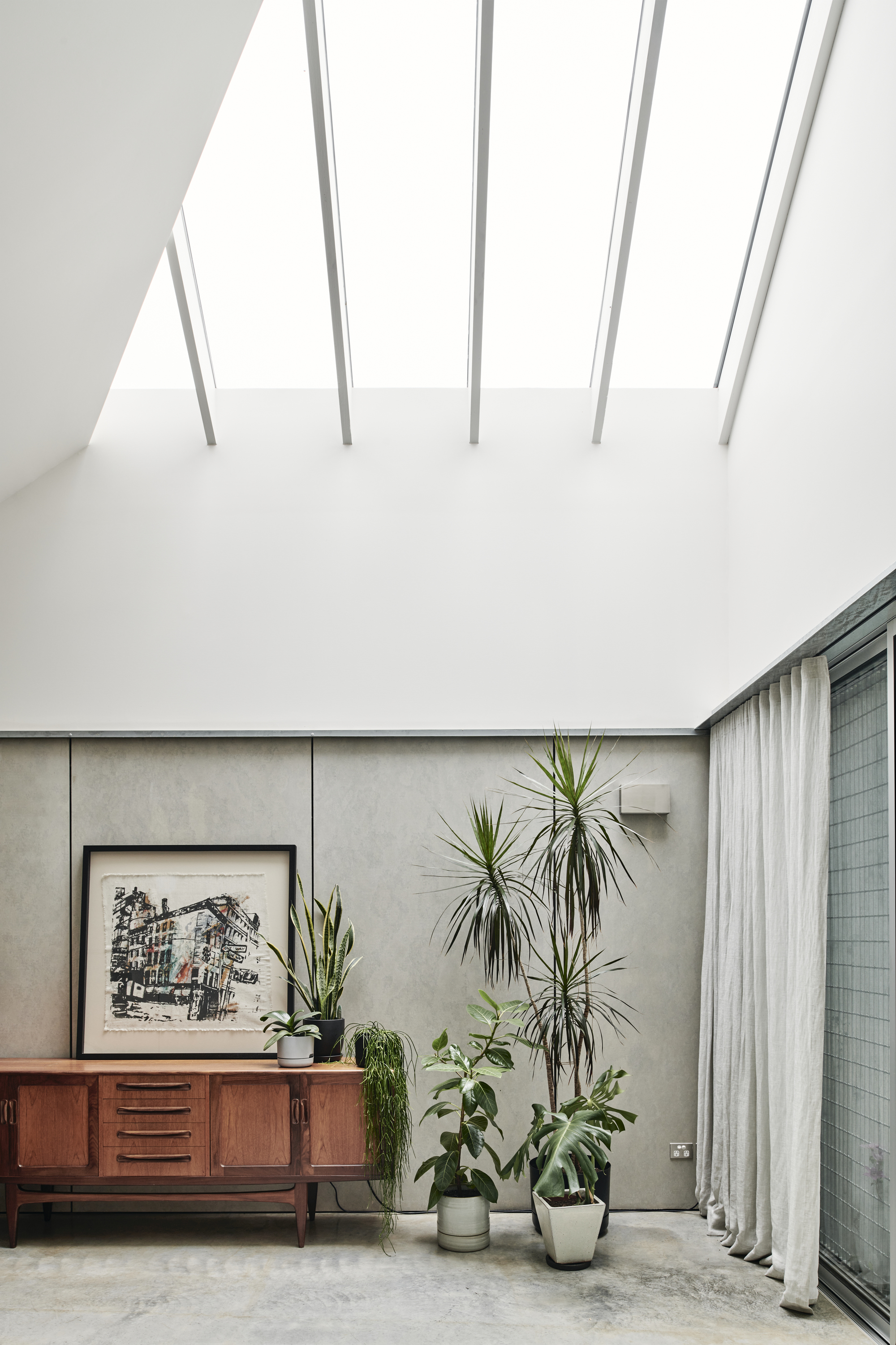 Corner detail showing concrete panel wall with potted plants beneath skylight apertures in sloped ceiling